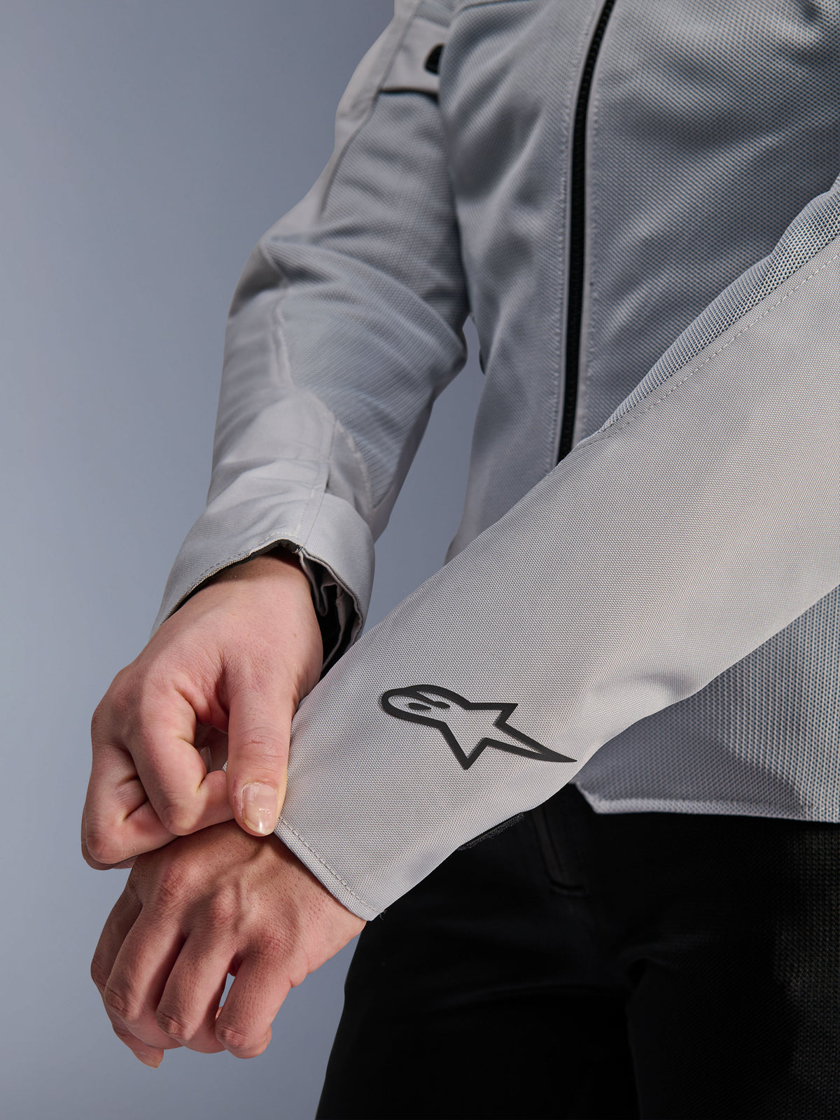 Zbliżenie na kurtkę Alpinestars Stella C-1 Air w kolorze srebrnym, z konstrukcją z technicznej siatki i czarnym logo Alpinestars na lewym rękawie, miejska kurtka motocyklowa dla kobiet z odblaskowym brandingiem.