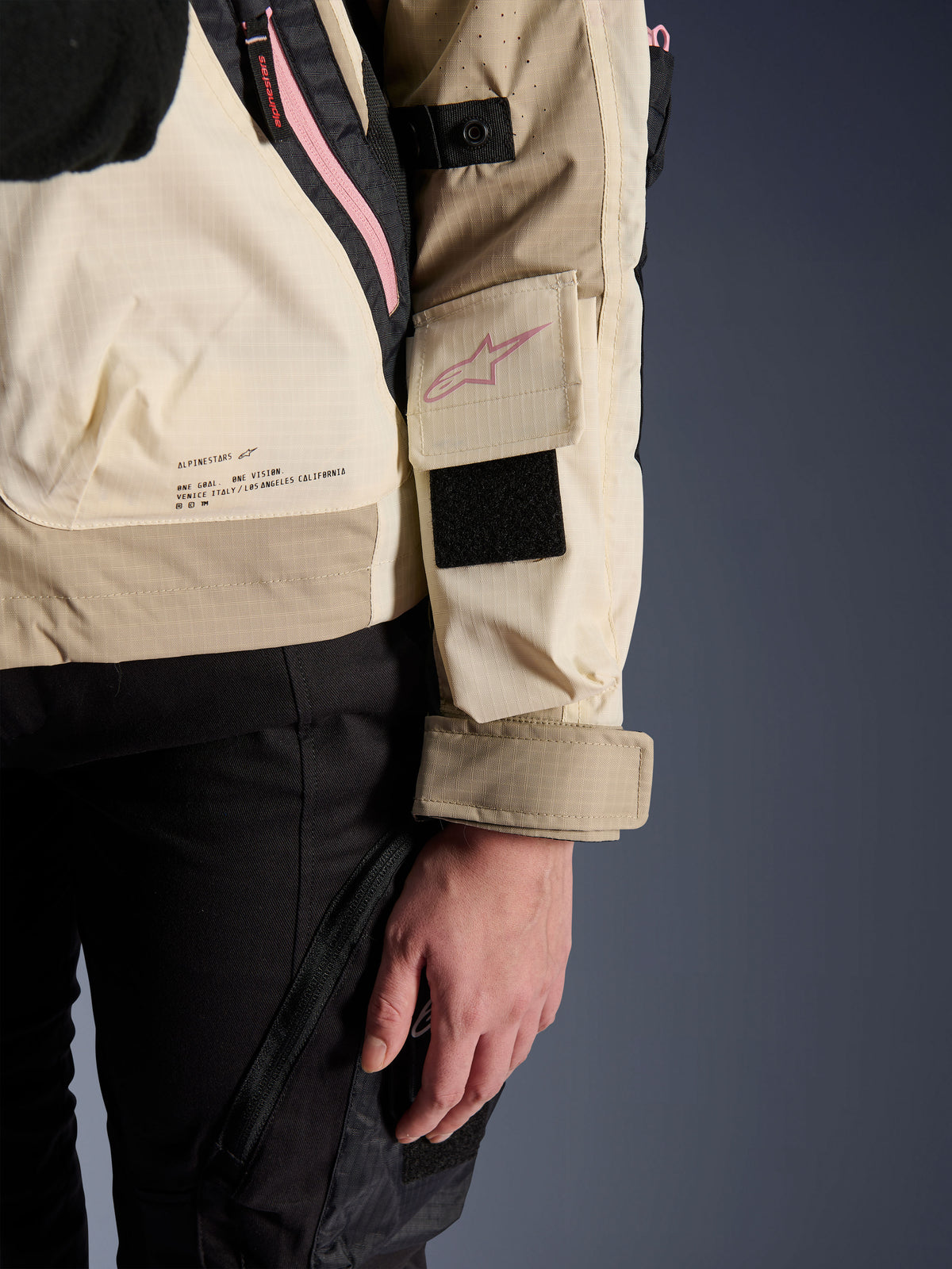 Alpinestars Molly Air Jacket, damska miejska kurtka motocyklowa, Sand Pink Almond, zbliżenie z boku pokazujące kieszeń na rękawie z różowym logo, czarny rzep i tekst z misją marki na dole pleców, lekki materiał ripstop