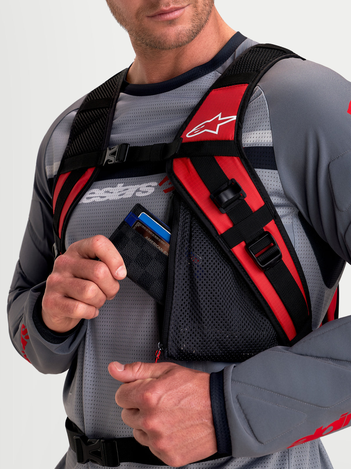 Alpinestars Plecak AT-9, plecak motocyklowy MX, czarny i jaskrawo czerwony, widok z bliska na wyściełany system szelek i zapinaną na zamek siatkową kieszeń na akcesoria noszoną przez modela