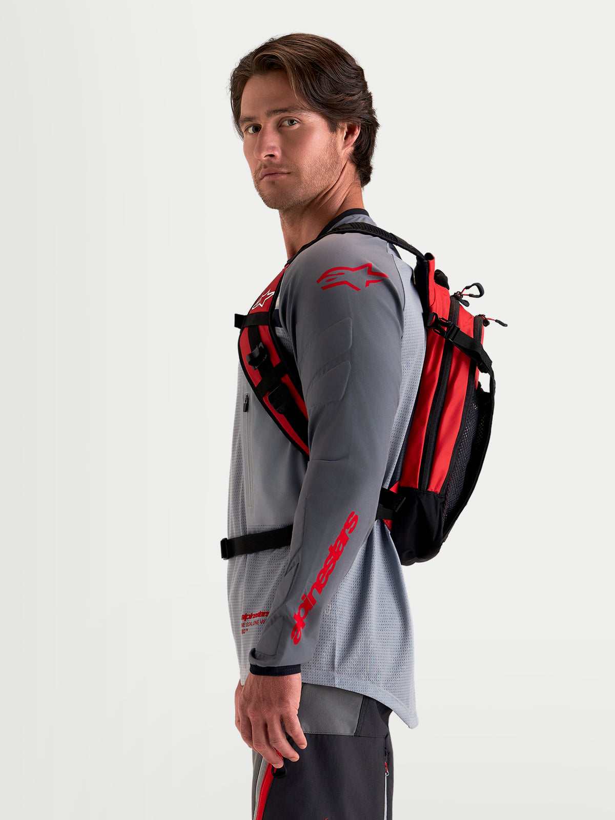 Alpinestars Plecak AT-9, plecak motocyklowy motocross, czarny i jaskrawo czerwony, widok z boku na modela w pasującym stroju MX, z lekką konstrukcją tekstylną i ergonomicznym systemem nośnym
