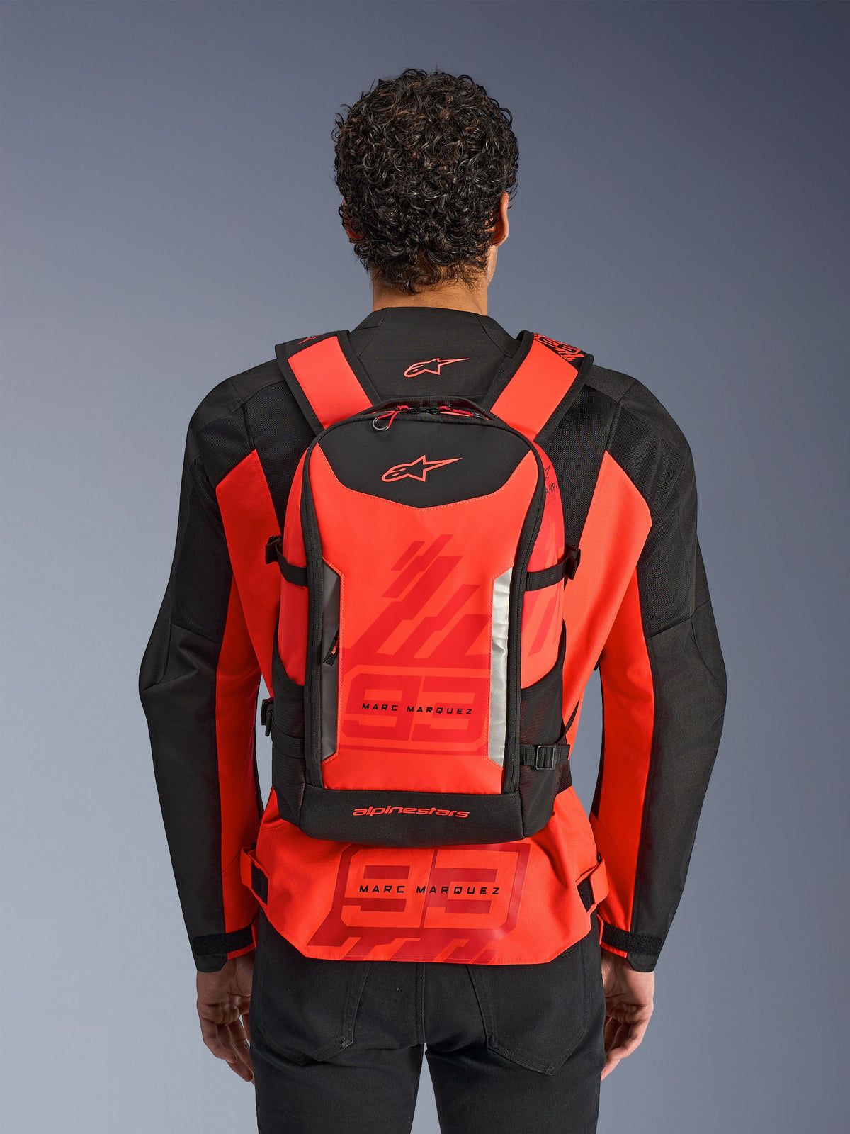 Alpinestars MM93 AMP3 Backpack, Technical Motorcycle Backpack, Red Fluo and Black, worn by a rider from behind over a matching red and black MM93 racing jacket, featuring Marc Marquez branding and Alpinestars logos.