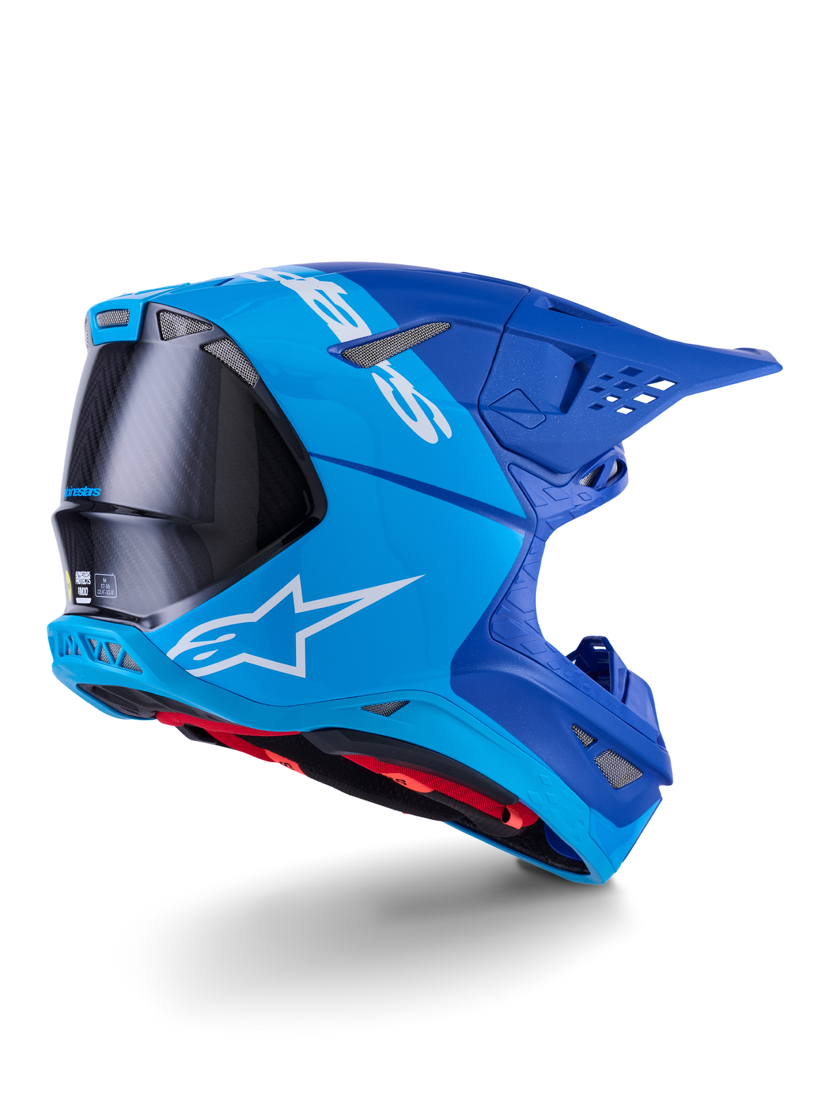 Kask Alpinestars Supertech M10 Flood, kask motocrossowy, jasnoniebieski i granatowy z widocznym czarnym włóknem węglowym, profil tylno-boczny pokazujący otwory wentylacyjne i białe logo, czerwona wyściółka, zaawansowana konstrukcja aerodynamiczna do jazdy w terenie