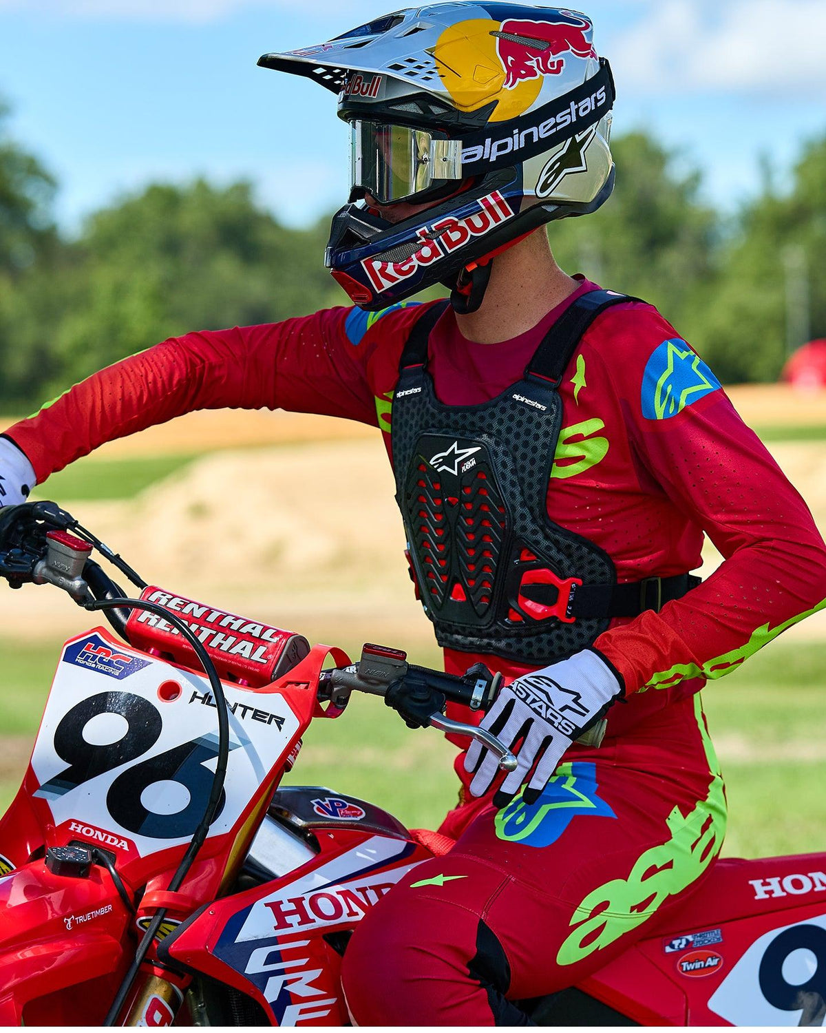 Motocross rider wearing Alpinestars A-5 Plasma Chest Protector in Black and Red, paired with a red and lime green racing jersey and pants, seated on a red Honda motorcycle, high-performance off-road protective gear