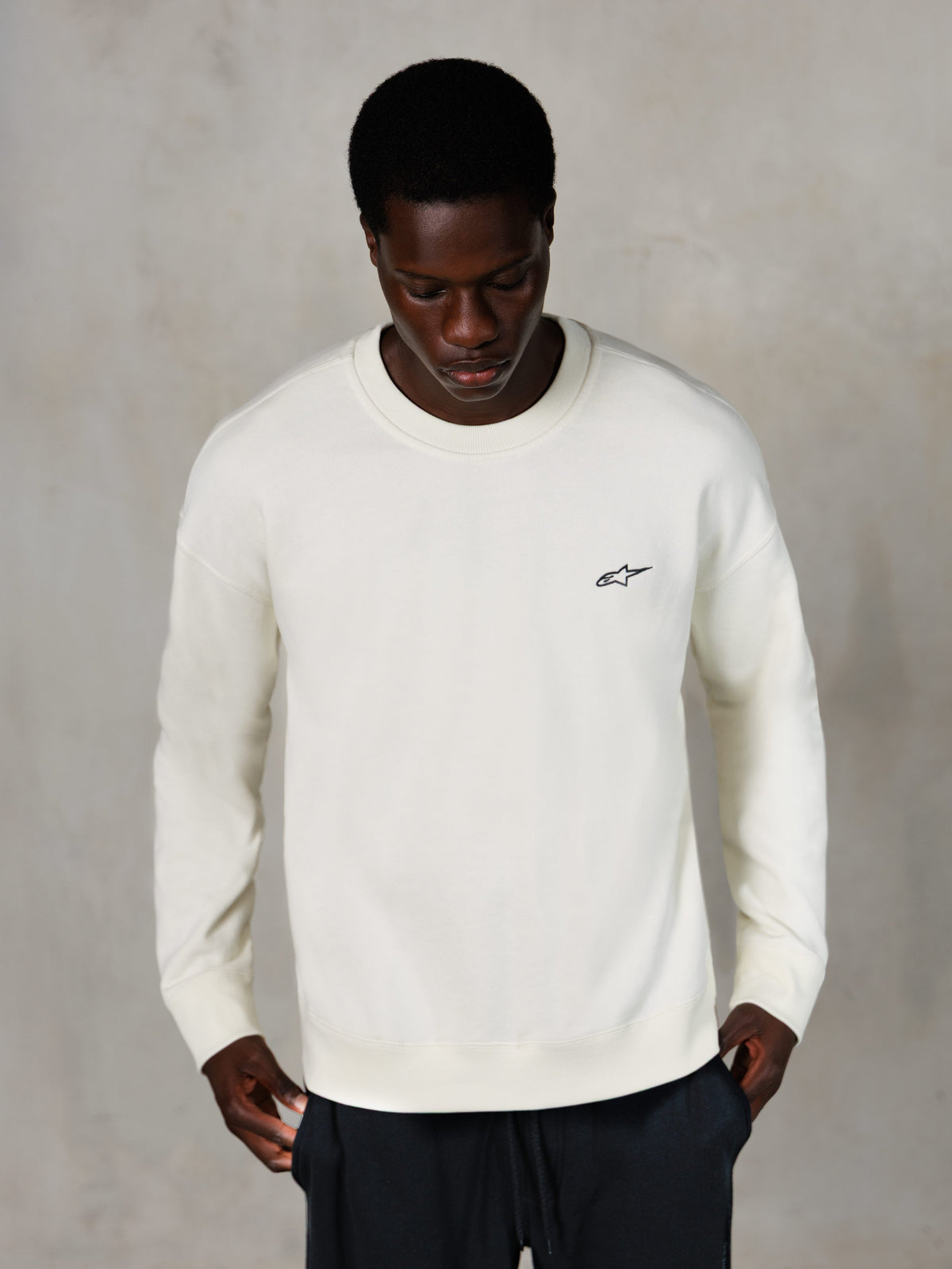Alpinestars Essentials Ageless Crew, bluza z okrągłym dekoltem, kolor Off White, małe czarne logo Alpinestars na piersi, noszona przez modela, casualowa odzież streetwear, miękki polar premium