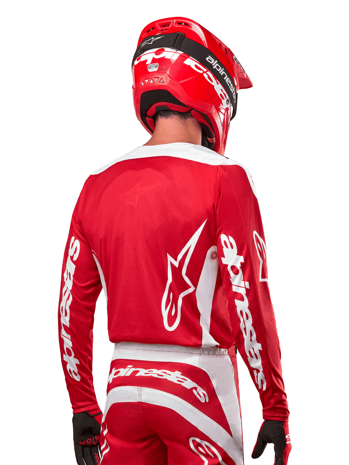 Kierowca motocrossowy w koszulce Alpinestars 2024 Fluid Lurv, kolor czerwono-biały, widok z tyłu ukazujący białe logo Alpinestars na plecach i branding na rękawach, w zestawie z dopasowanym czerwonym kaskiem i czarnymi rękawicami, profesjonalna odzież do wyścigów off-road
