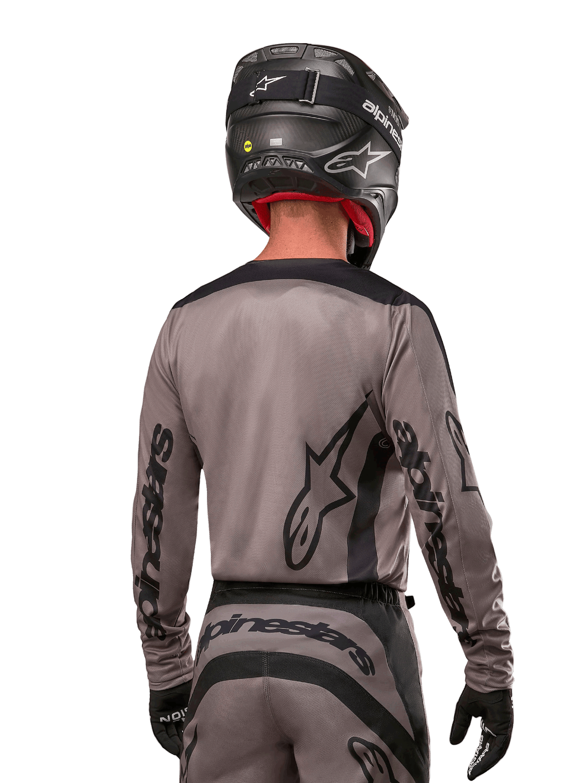 Motocyklista motocrossowy widziany od tyłu w koszulce Alpinestars 2024 Fluid Lurv w kolorze Mud Black, czarne logo Alpinestars na rękawach i plecach, czarny kask i dopasowany sprzęt do wyścigów terenowych