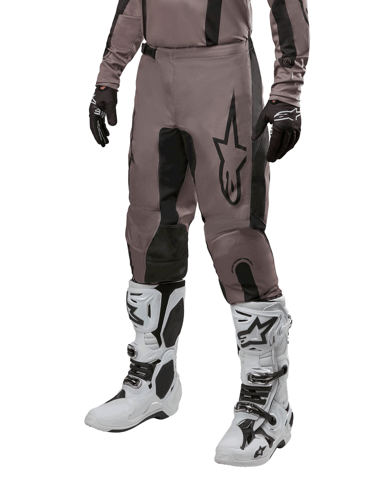 Alpinestars 2024 Fluid Lurv Pants, spodnie motocrossowe, kolor Mud Black i czarny, z logo Alpinestars, noszone z czarnymi rękawicami i białymi butami motocrossowymi, sportowy design do wyścigów terenowych