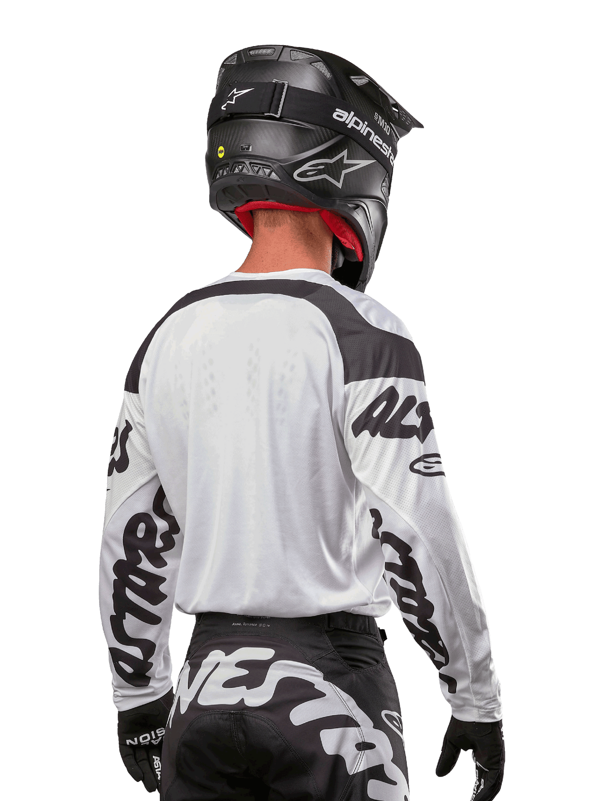 Koszulka Alpinestars Racer Hana 2024, biało-czarna, widok z tyłu prezentujący ergonomiczny krój i wyraźne logo na rękawach, zestawiona z czarnym kaskiem motocrossowym i pasującymi czarno-białymi spodniami, profesjonalny sprzęt wyścigowy do jazdy terenowej