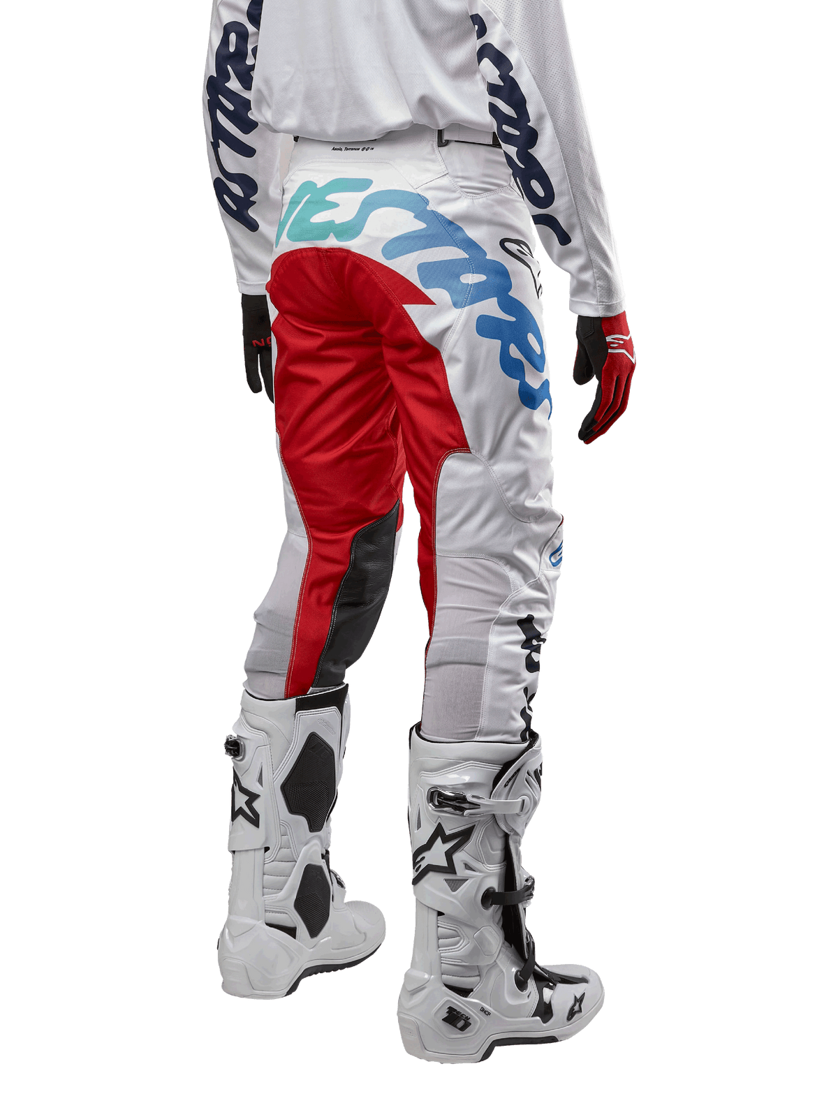 Alpinestars Racer Hana Pants 2024, spodnie motocrossowe, wielokolorowe białe z czerwonymi i niebieskimi akcentami, widok z tyłu pokazujący duże logo na siedzeniu, noszone z biało-czarnymi butami motocrossowymi, zaprojektowane dla wydajności i trwałości w terenie