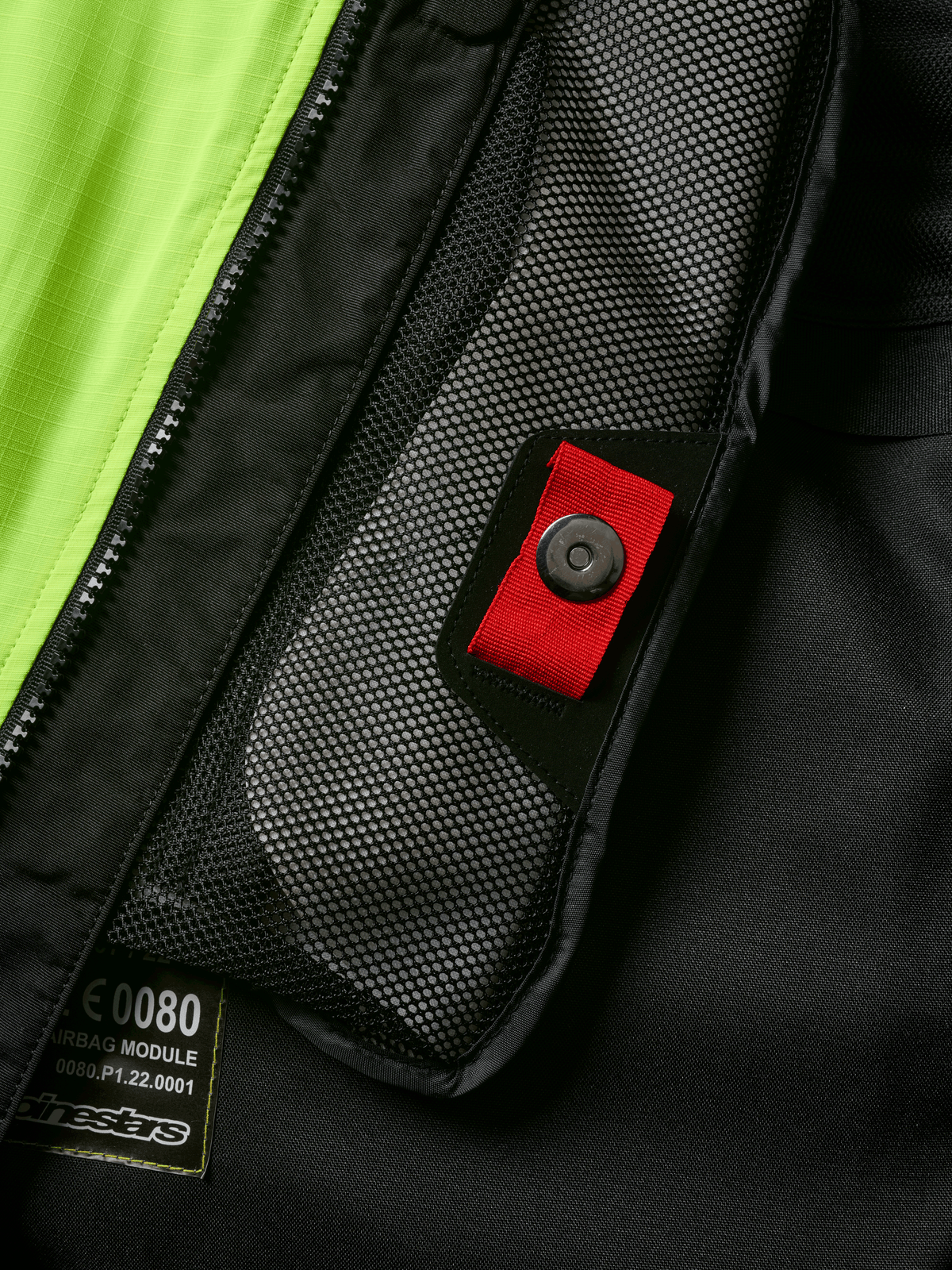 Alpinestars Tech-Air® 3 V2 System, zbliżenie na detal wewnętrznej kieszeni z siatki z czerwonym uchwytem i zatrzaskiem, jaskrawożółty panel fluo, czarna konstrukcja tekstylna z widoczną etykietą modułu poduszki powietrznej i zamkiem błyskawicznym