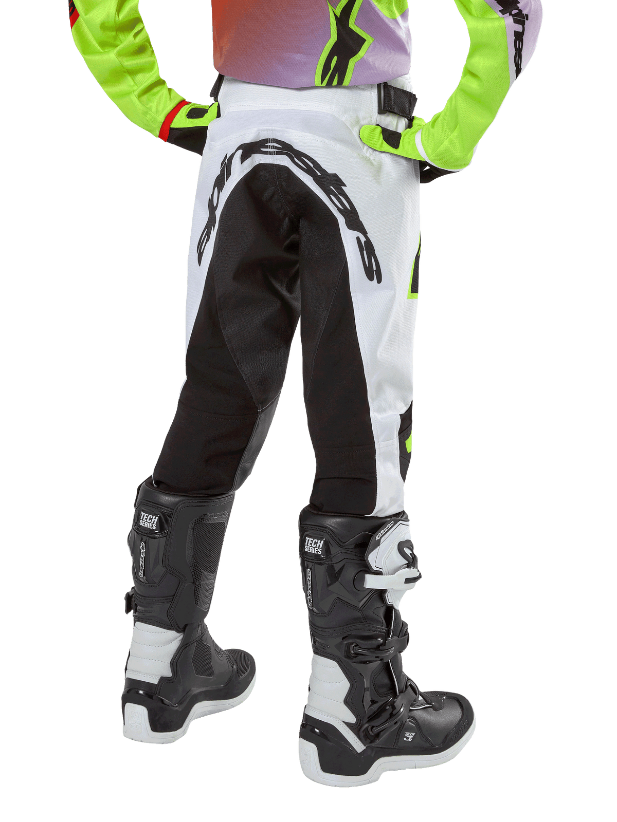 Alpinestars Youth 2024 Racer Lucent Pants, spodnie motocrossowe, biało-czarne z neonowymi akcentami, widok z tyłu ukazujący duży elastyczny panel oraz logo Alpinestars, noszone z czarno-białymi butami Alpinestars Tech Series