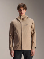 Alpinestars A-Dura Rain Jacket, jasnobrązowa kurtka przeciwdeszczowa z kapturem na rower górski, prezentowana przez modela, małe logo na piersi, regulowane paski przy mankietach i ukryty przedni zamek błyskawiczny, wodoodporna odzież rowerowa