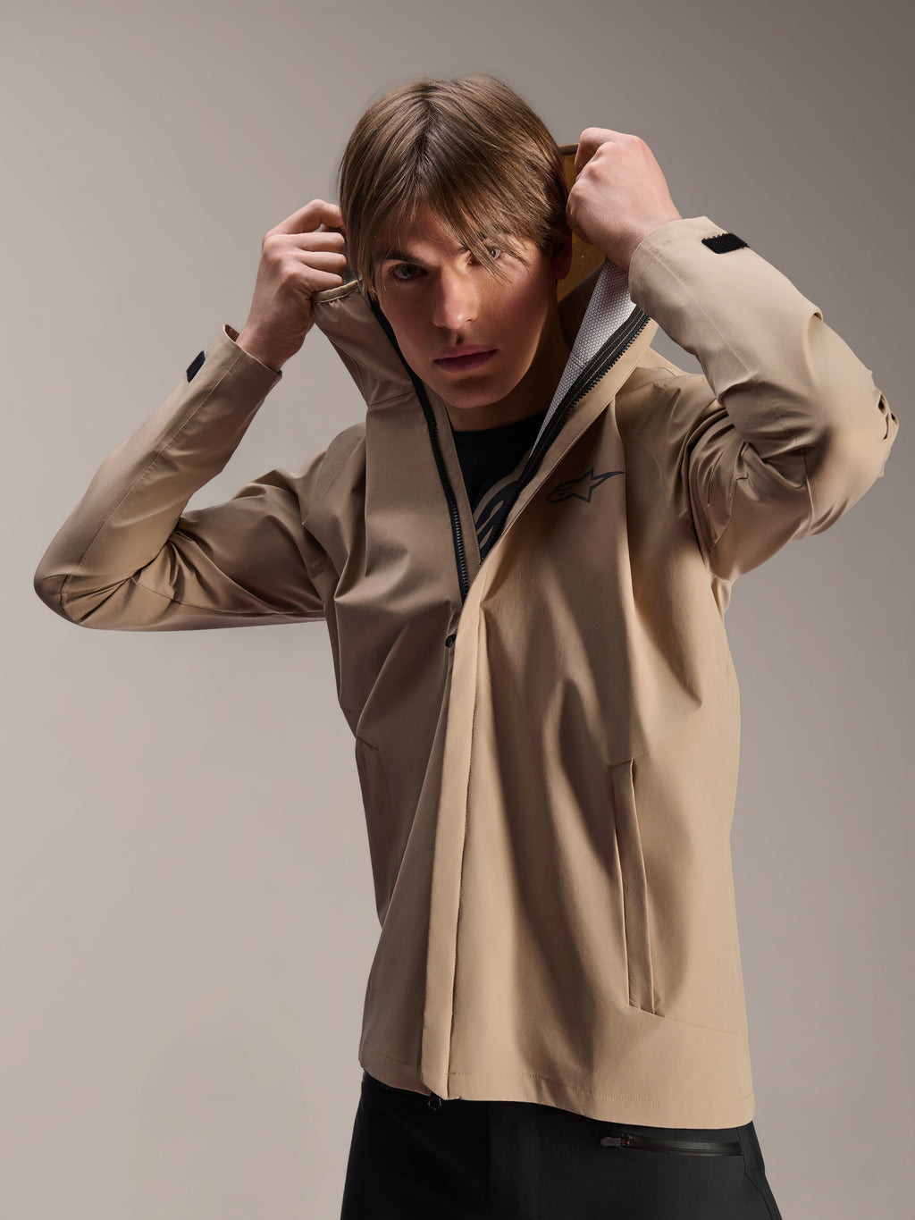 Alpinestars A-Dura Rain Jacket, kurtka rowerowa MTB, jasnobrązowa, model w kurtce naciągający elastyczny kaptur, czarne logo na piersi, kieszenie na zamek, techniczna 2,5-warstwowa wodoodporna tkanina