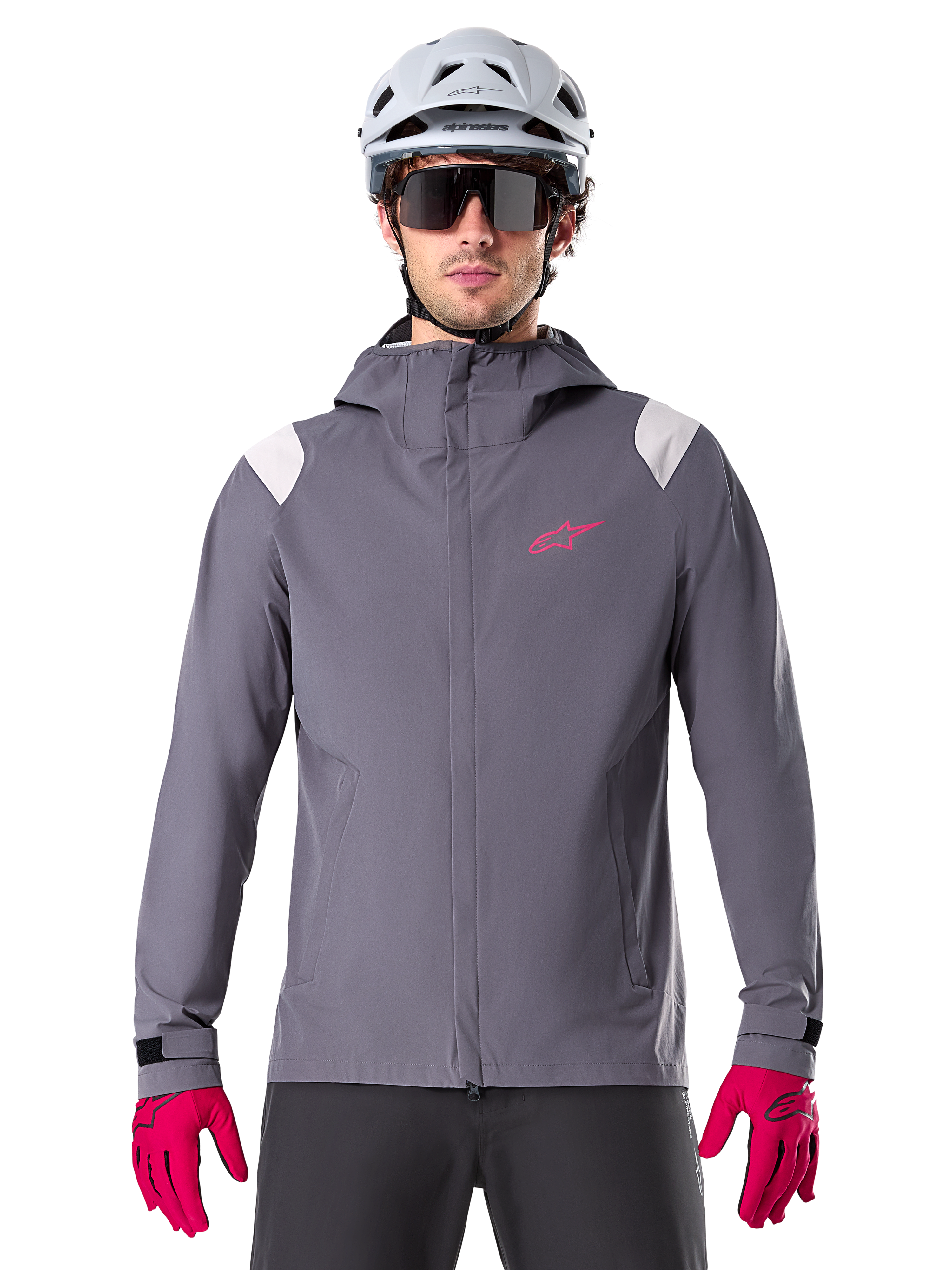Kurtka przeciwdeszczowa Alpinestars A-Dura, rowerowa kurtka przeciwdeszczowa MTB, kolor ciemny tytanowy szary, fason z kapturem z różowym logo Alpinestars i jasnoszarymi panelami na ramionach, noszona z białym kaskiem MTB i jaskraworóżowymi rękawiczkami, wodoodporna odzież do jazdy w terenie