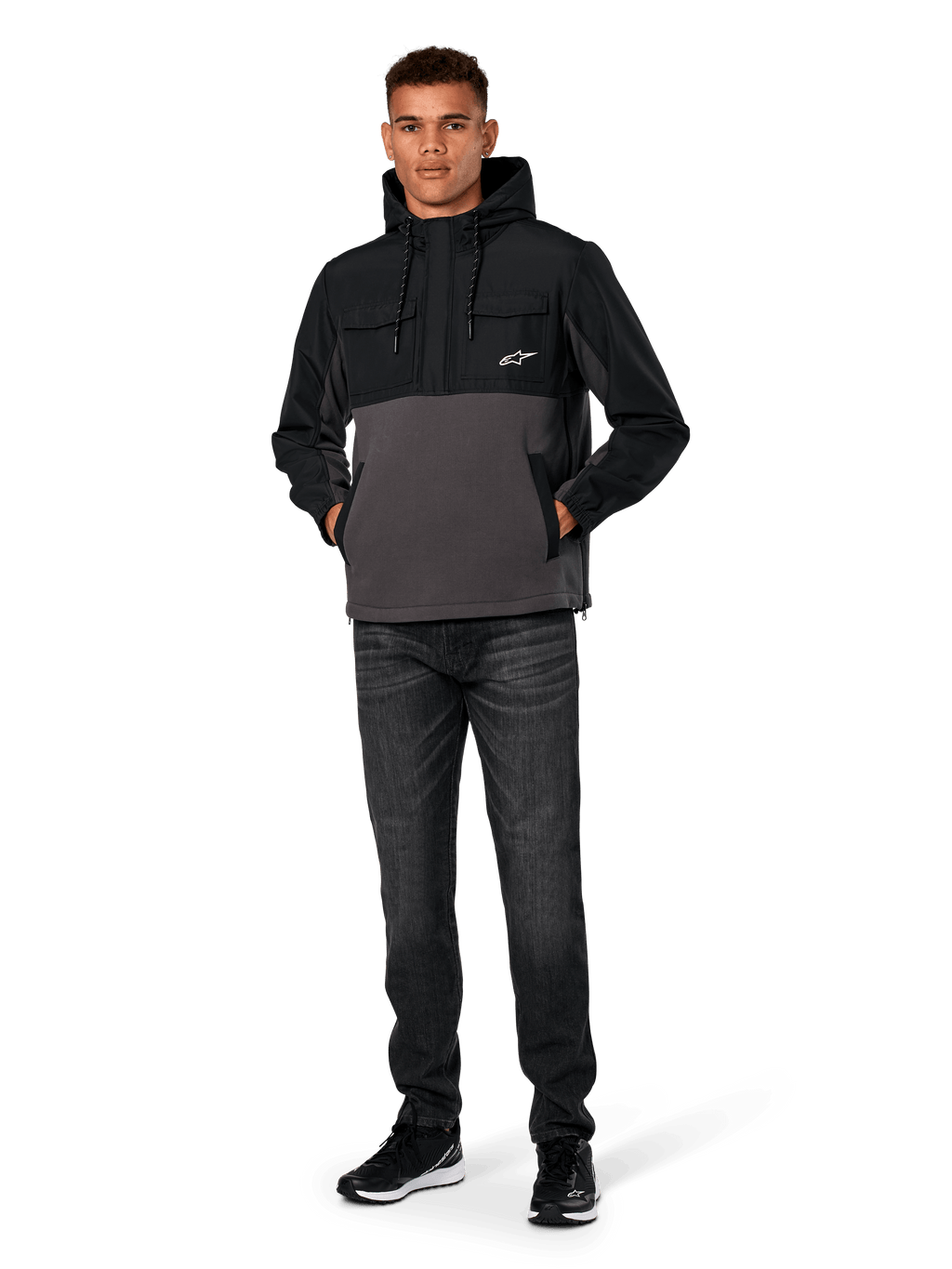 Kurtka Alpinestars Juncture Hybrid, czarno-szara (Gunmetal), anorak z kapturem z mieszanych materiałów z polarem płóciennym i nakładkami ripstop, białe logo A-star na piersi, kaptur ze sznurkiem, model w ciemnych dżinsach i czarnych sneakersach, codzienna odzież uliczna inspirowana motorsportem