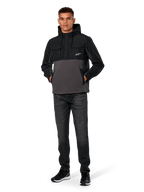 Kurtka Alpinestars Juncture Hybrid, czarno-szara (Gunmetal), anorak z kapturem z mieszanych materiałów z polarem płóciennym i nakładkami ripstop, białe logo A-star na piersi, kaptur ze sznurkiem, model w ciemnych dżinsach i czarnych sneakersach, codzienna odzież uliczna inspirowana motorsportem