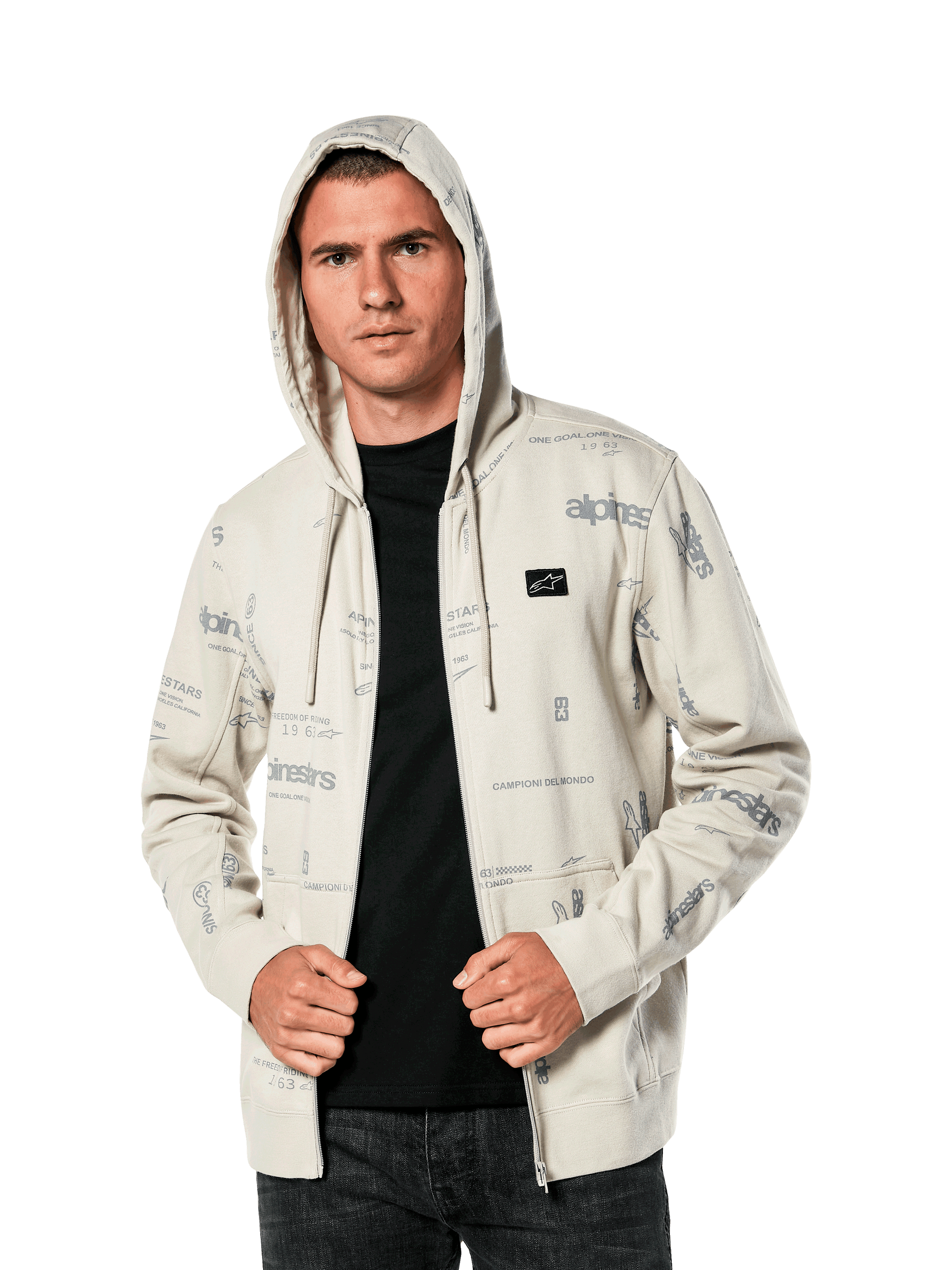Alpinestars Plenitude Hoodie, casualowa odzież sportowa, polarowa bluza w kolorze złamanej bieli rozpinana na zamek, szare grafiki logo na całej powierzchni, noszona przez mężczyznę z założonym kapturem na czarną koszulkę, mała naszywka z logo na piersi i kieszeń typu kangurek