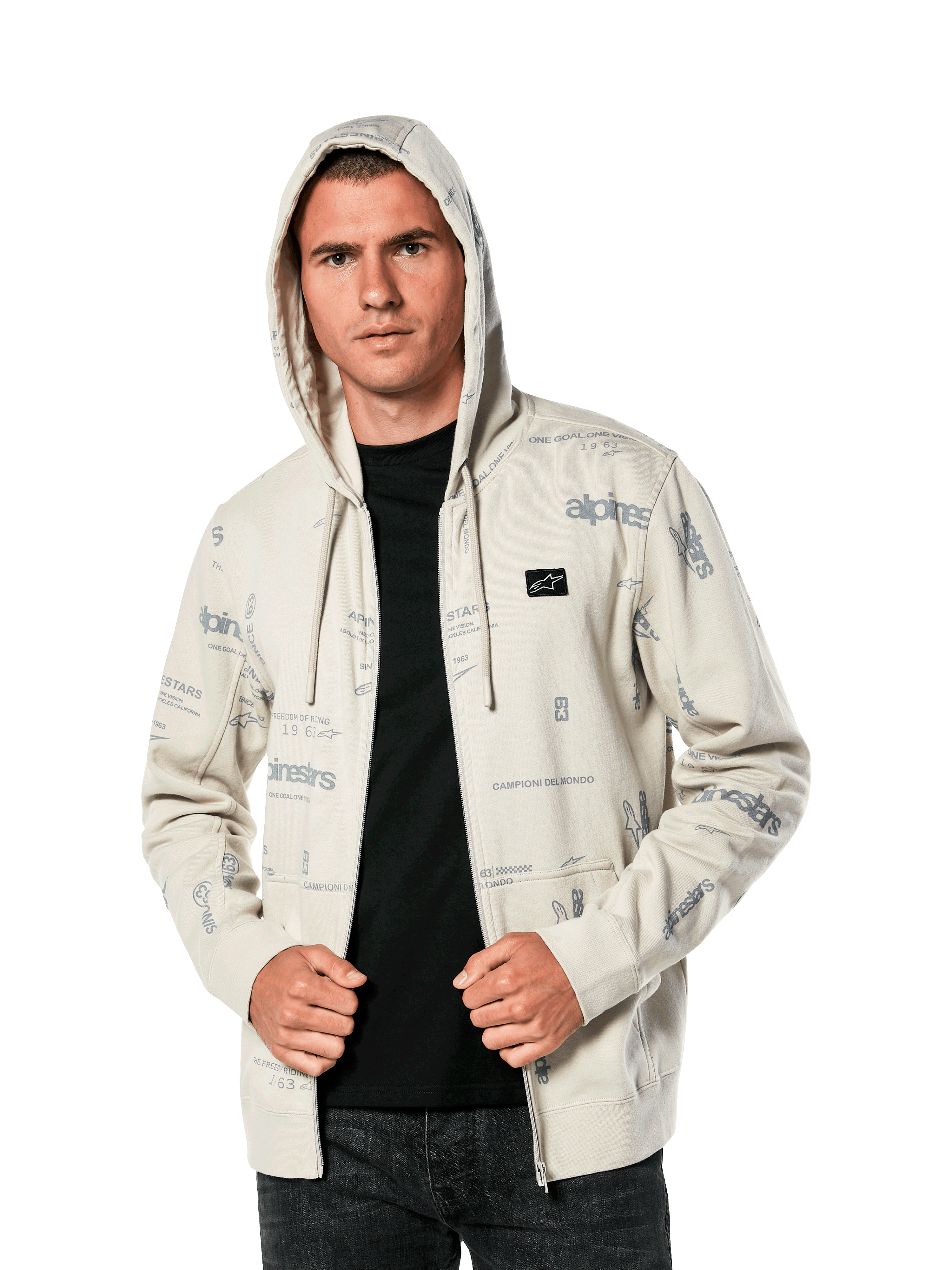 Alpinestars Plenitude Hoodie, casualowa odzież sportowa, polarowa bluza w kolorze złamanej bieli rozpinana na zamek, szare grafiki logo na całej powierzchni, noszona przez mężczyznę z założonym kapturem na czarną koszulkę, mała naszywka z logo na piersi i kieszeń typu kangurek