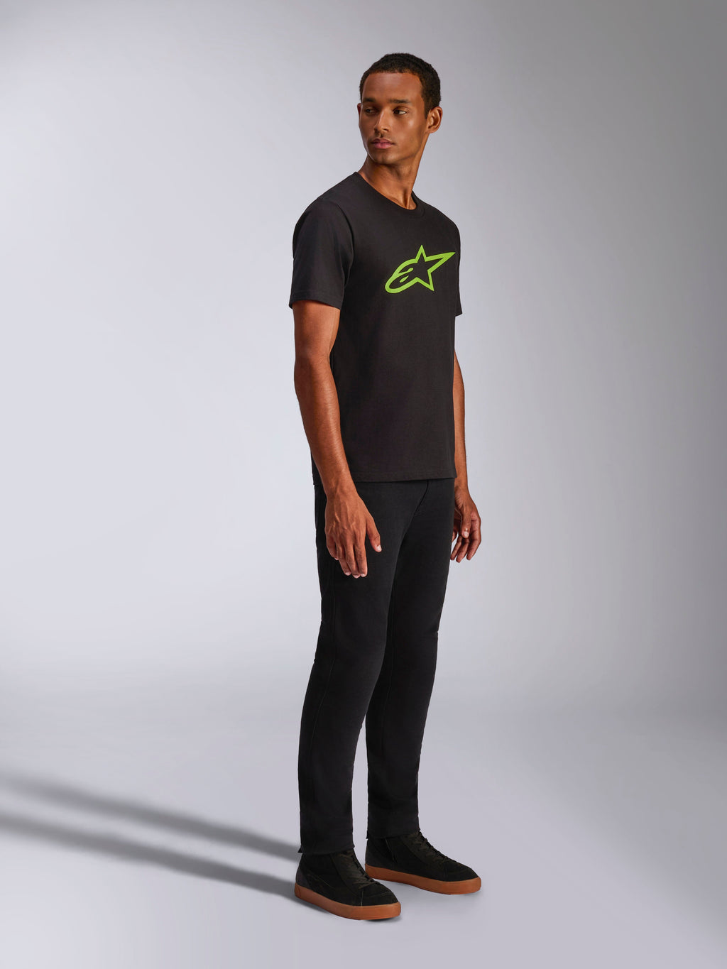Alpinestars Ageless 2.0 CSF Tee, koszulka z krótkim rękawem, czarna z jasnozielonym logo Alpinestars, zestawiona z czarnymi spodniami i sneakersami, codzienna odzież uliczna inspirowana sportami motorowymi