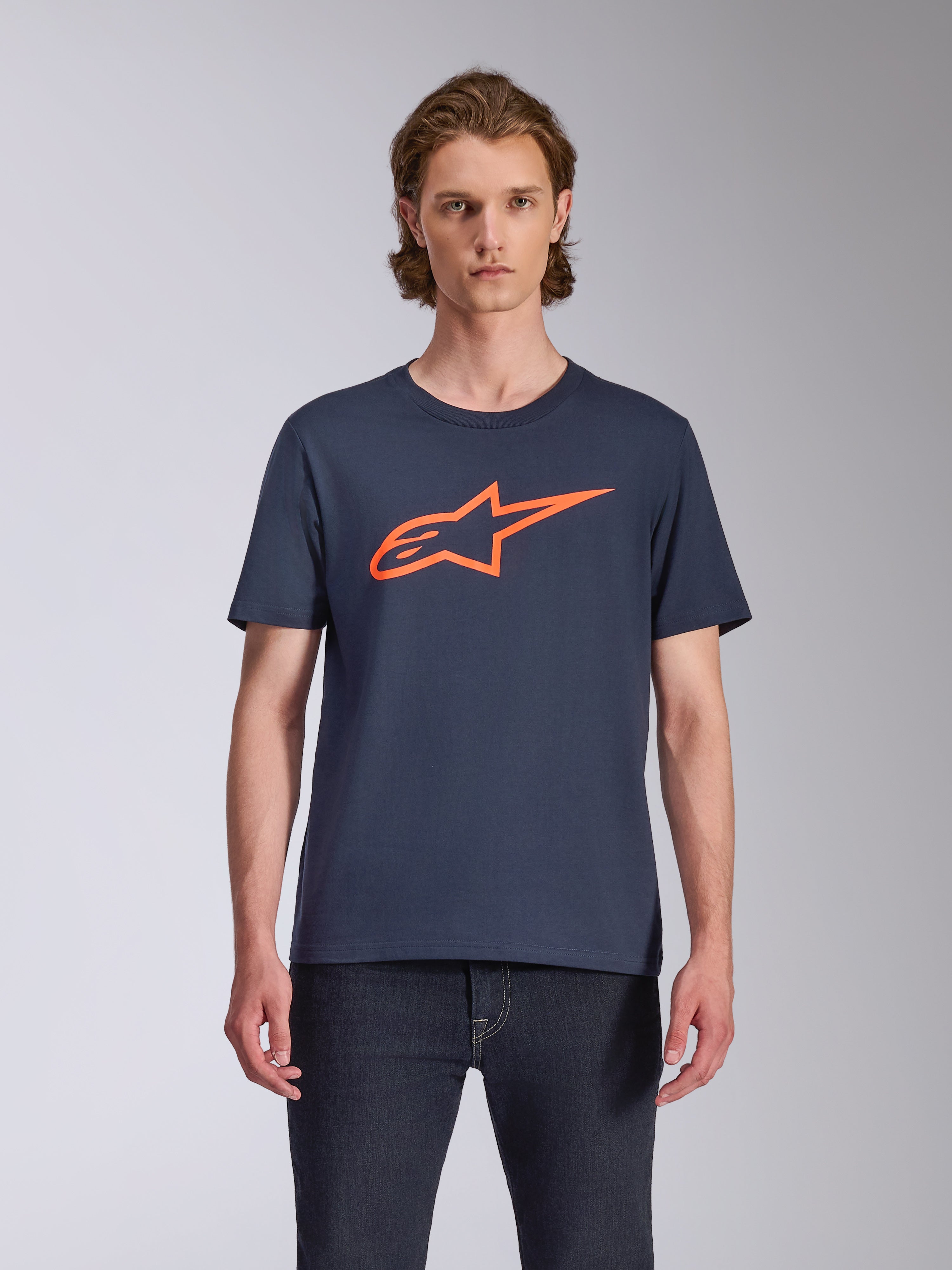 Alpinestars Ageless 2.0 CSF Tee, koszulka z krótkim rękawem, granatowa z jasnopomarańczowym logo, noszona z ciemnymi jeansami, casualowa odzież lifestylowa w stylu motorsportowym
