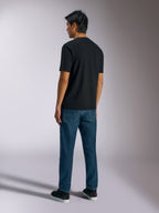 Alpinestars Ageless Shadow CSF Tee, koszulka z krótkim rękawem, czarna, widok z tyłu, noszona z niebieskimi jeansami i czarnymi sneakersami, codzienna odzież uliczna inspirowana motorsportem