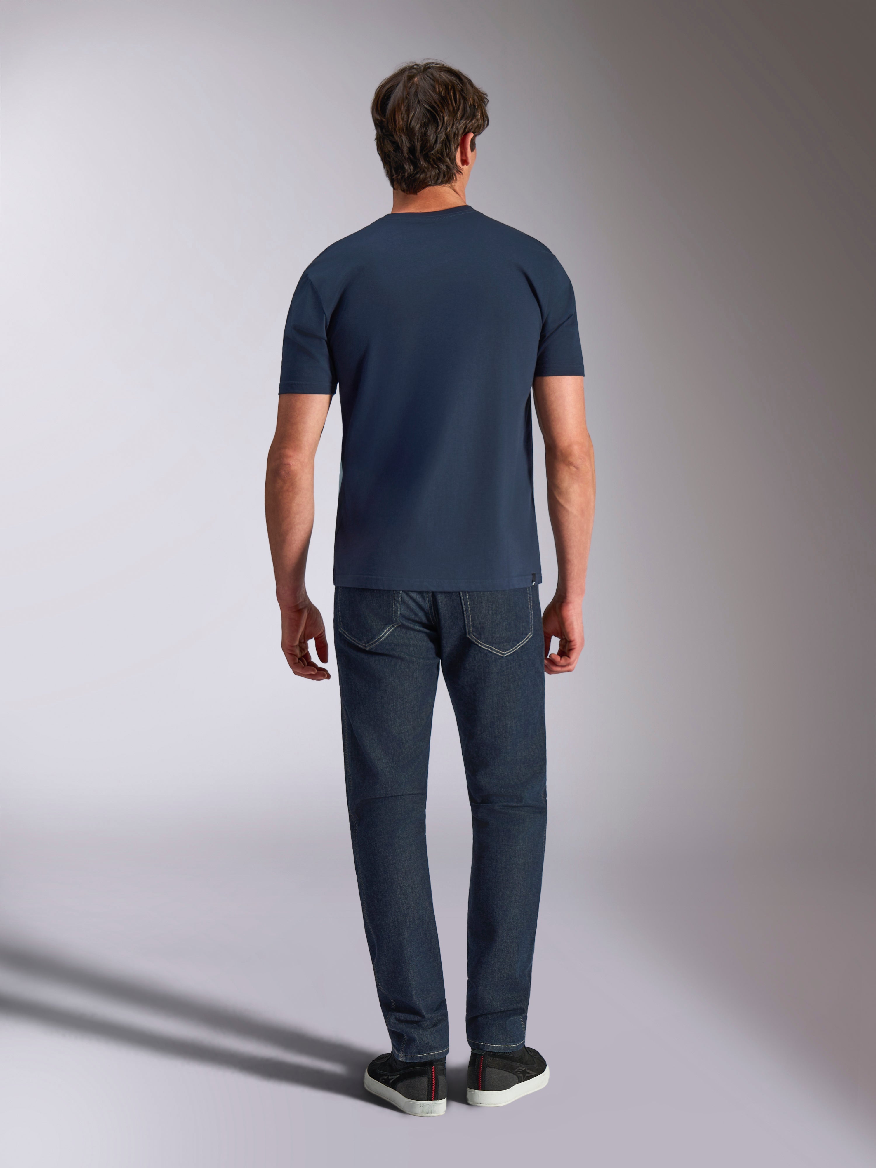 Alpinestars Ageless Shadow CSF Tee, koszulka z krótkim rękawem, granatowa, widok z tyłu na modela w ciemnych dżinsach i czarnych sneakersach, codzienna odzież uliczna w stylu motorsport