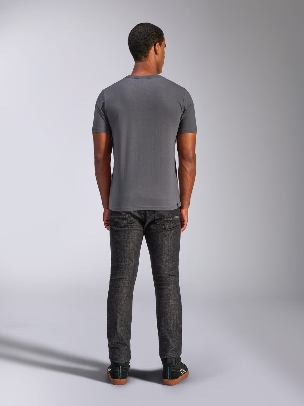 Alpinestars Always 2.0 CSF Tee, koszulka z krótkim rękawem, ciemnoszara, widok z tyłu, noszona z ciemnymi jeansowymi spodniami, codzienna odzież uliczna inspirowana sportami motorowymi