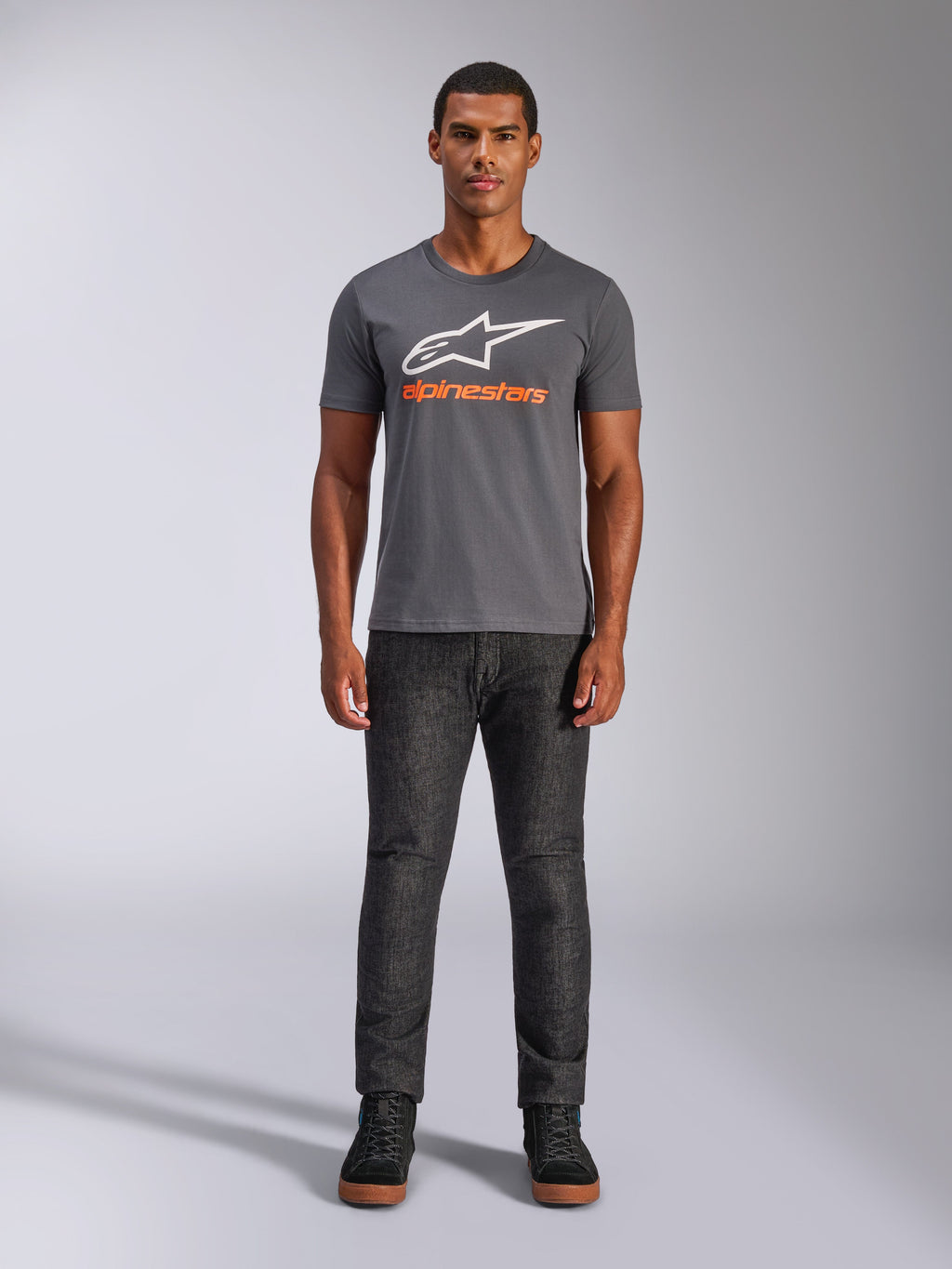 Alpinestars Always 2.0 CSF Tee, t-shirt z krótkim rękawem, grafitowy z białym logo i pomarańczowym napisem, prezentowany przez modela w ciemnych dżinsach, codzienna odzież streetwearowa w stylu motorsportowym