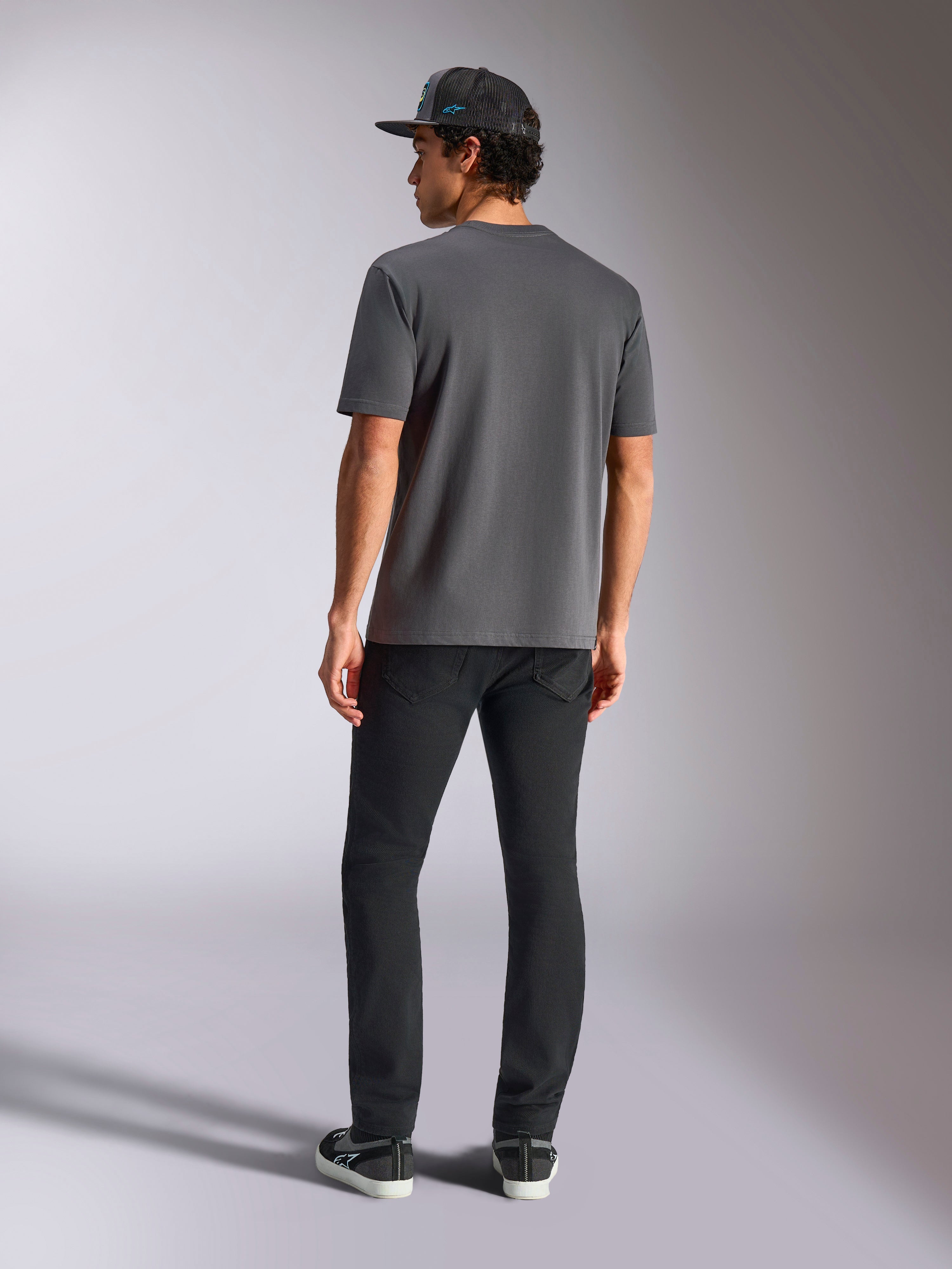Alpinestars Blaze 2.0 CSF Tee, ciemnoszara koszulka z krótkim rękawem, widok z tyłu, noszona z czarnymi spodniami i czarną czapką z daszkiem typu mesh, codzienna odzież streetwearowa w stylu motorsport