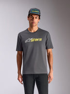 Alpinestars Blaze 2.0 CSF Tee, t-shirt z krótkim rękawem, grafitowy, białe logo gwiazdy i żółta neonowa grafika stars, noszony z dopasowaną czapką typu trucker i czarnymi spodniami, casualowa odzież uliczna w stylu motorsport