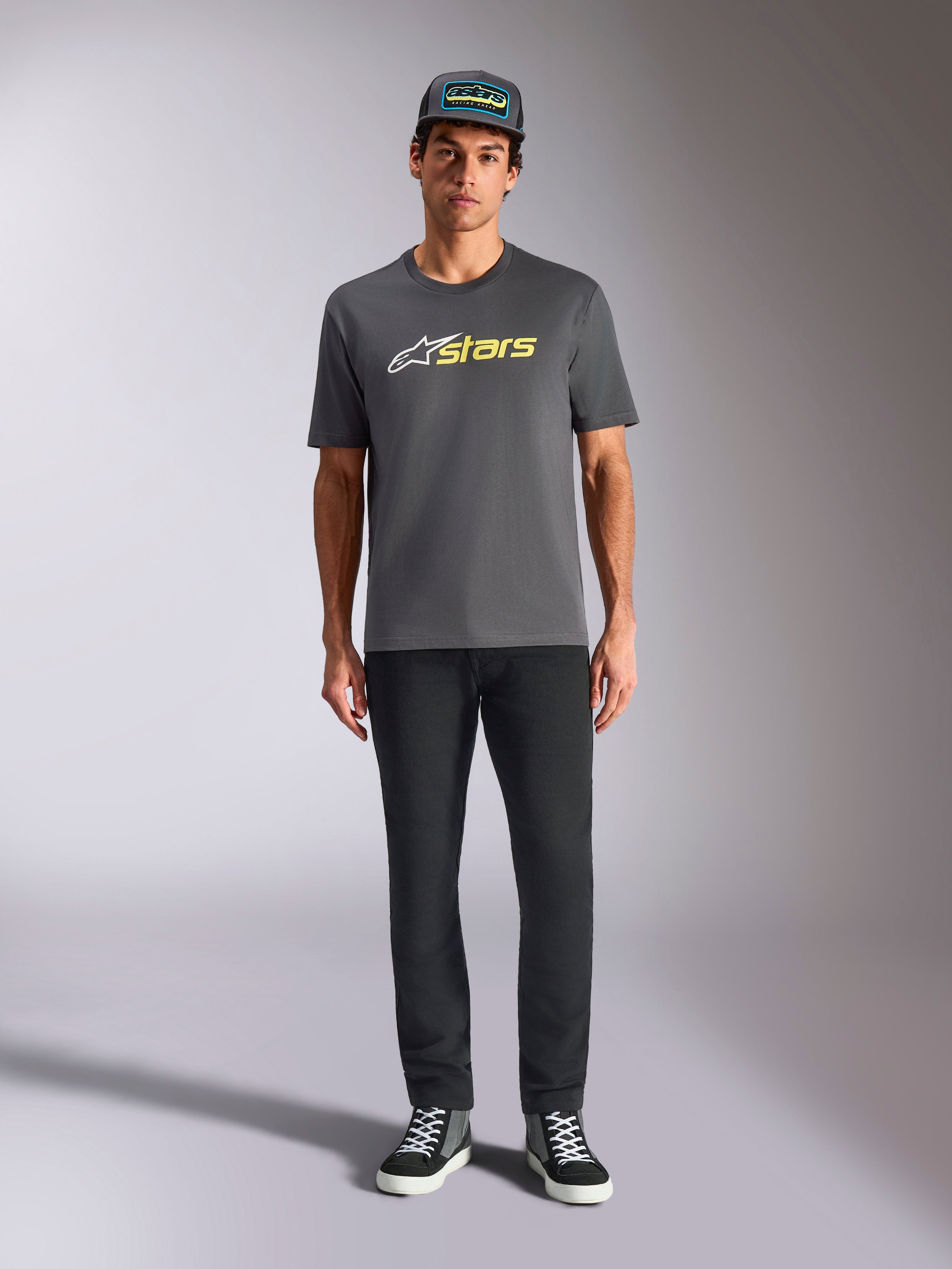 Alpinestars Blaze 2.0 CSF Tee, koszulka z krótkim rękawem, ciemnoszara z biało-żółtym logo Hi-Vis, zestawiona z czarnymi spodniami i pasującą czapką typu trucker, codzienny styl motorsportowy