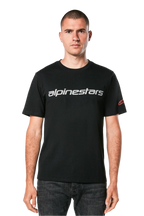 Koszulka Alpinestars Linear Wordmark 2.0 CSF, t-shirt z krótkim rękawem, czarny, szary linearny znak słowny na klatce piersiowej i czerwone logo Ageless na rękawie, noszona przez modela z ciemnymi jeansami, casualowy streetwear inspirowany sportami motorowymi