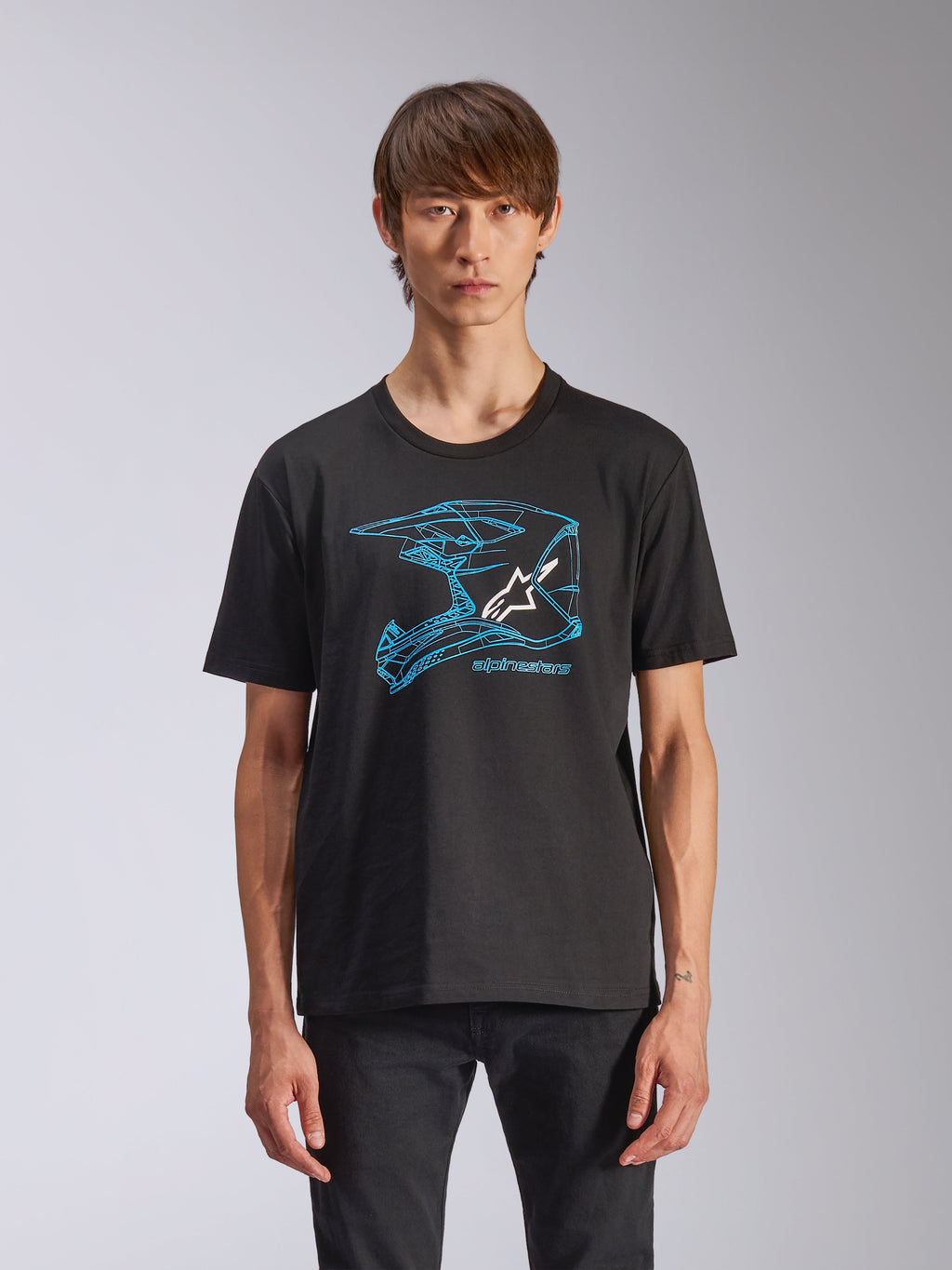 Alpinestars CSF Tee, czarna koszulka z krótkim rękawem, niebieska grafika przedstawiająca kask motocrossowy z białym logo Astars, codzienna odzież uliczna inspirowana sportami motorowymi, prezentowana przez modela