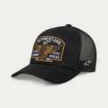 Alpinestars Heritage Patch Trucker Hat, czarna czapka typu trucker, usztywniona korona z zakrzywionym daszkiem, duża haftowana naszywka z przodu z uskrzydlonym kołem i napisem „Racing Ahead Est. 1963”, czarne panele z siatki z logo gwiazdy z boku, codzienne nakrycie głowy w stylu motorsport.