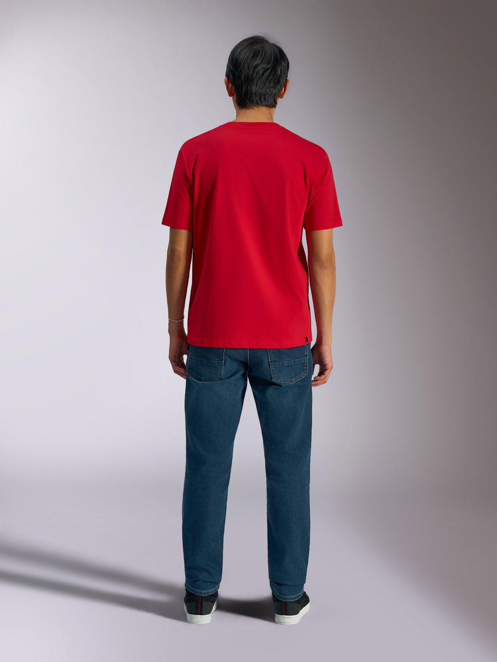 Alpinestars Ageless Shadow CSF Tee, widok z tyłu czerwonej koszulki z krótkim rękawem, zestawiona z ciemnoniebieskimi jeansami i czarnymi sneakersami, casualowy streetwear motorsportowy