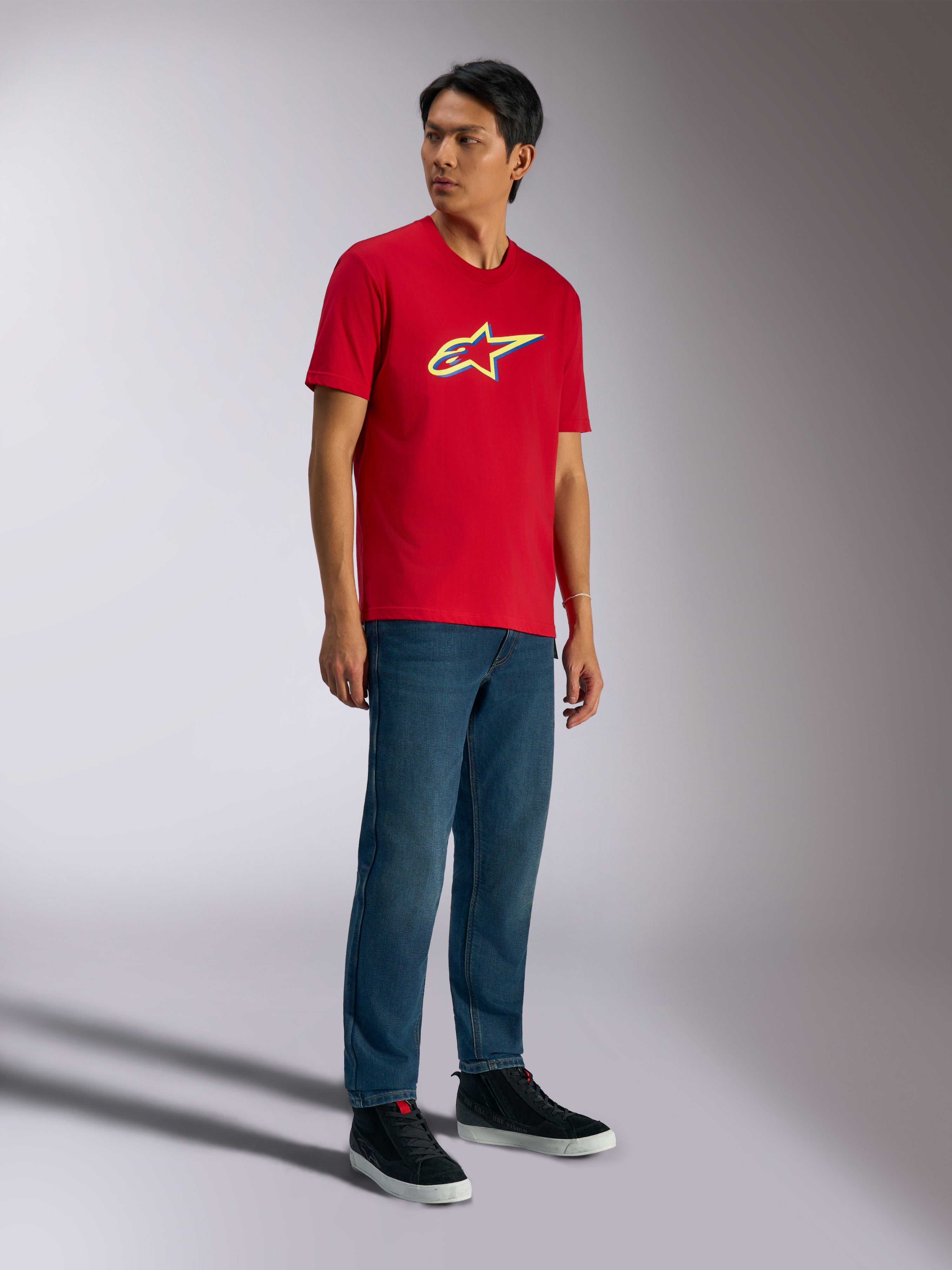 Alpinestars Ageless Shadow CSF Tee, koszulka z krótkim rękawem, czerwona, z logo Ageless shadow z żółtymi i niebieskimi akcentami, noszona przez modela z jeansami i czarnymi sneakersami, casualowa odzież streetwearowa
