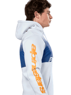 Alpinestars Specter Hoodie, casualowy streetwear, biała z niebieskim nadrukiem z efektem gradientu, duży pomarańczowy napis Alpinestars na rękawie, boczny profil mężczyzny w bluzie z kapturem