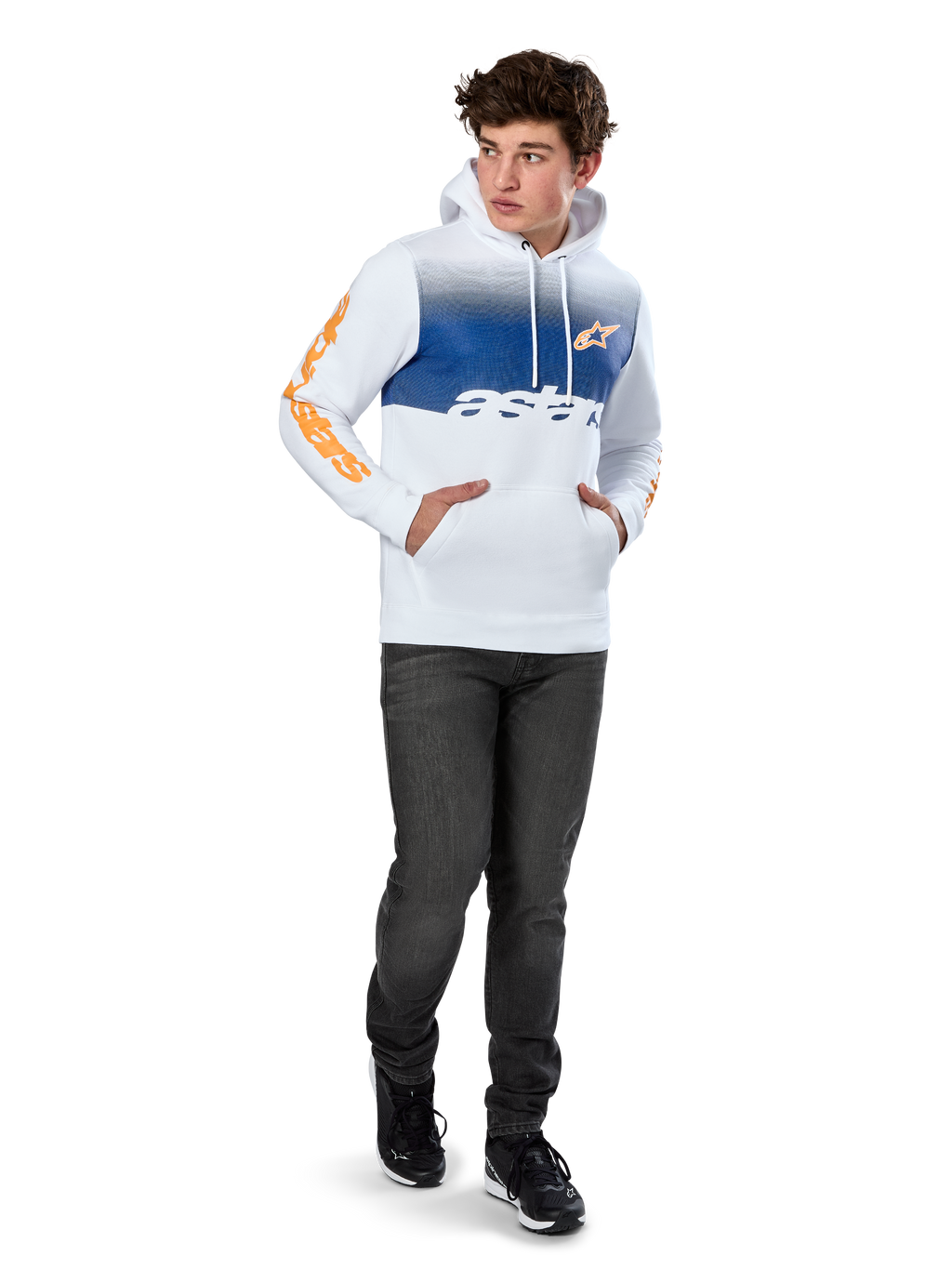 Alpinestars Specter Hoodie, biała bluza polarowa wkładana przez głowę z niebieskim cieniowanym nadrukiem, pomarańczowe logo HD z przodu i napisy na rękawach, z kieszenią typu kangurka i kapturem ściąganym sznurkiem, noszona z ciemnymi dżinsami w swobodnym stylu inspirowanym sportami motorowymi