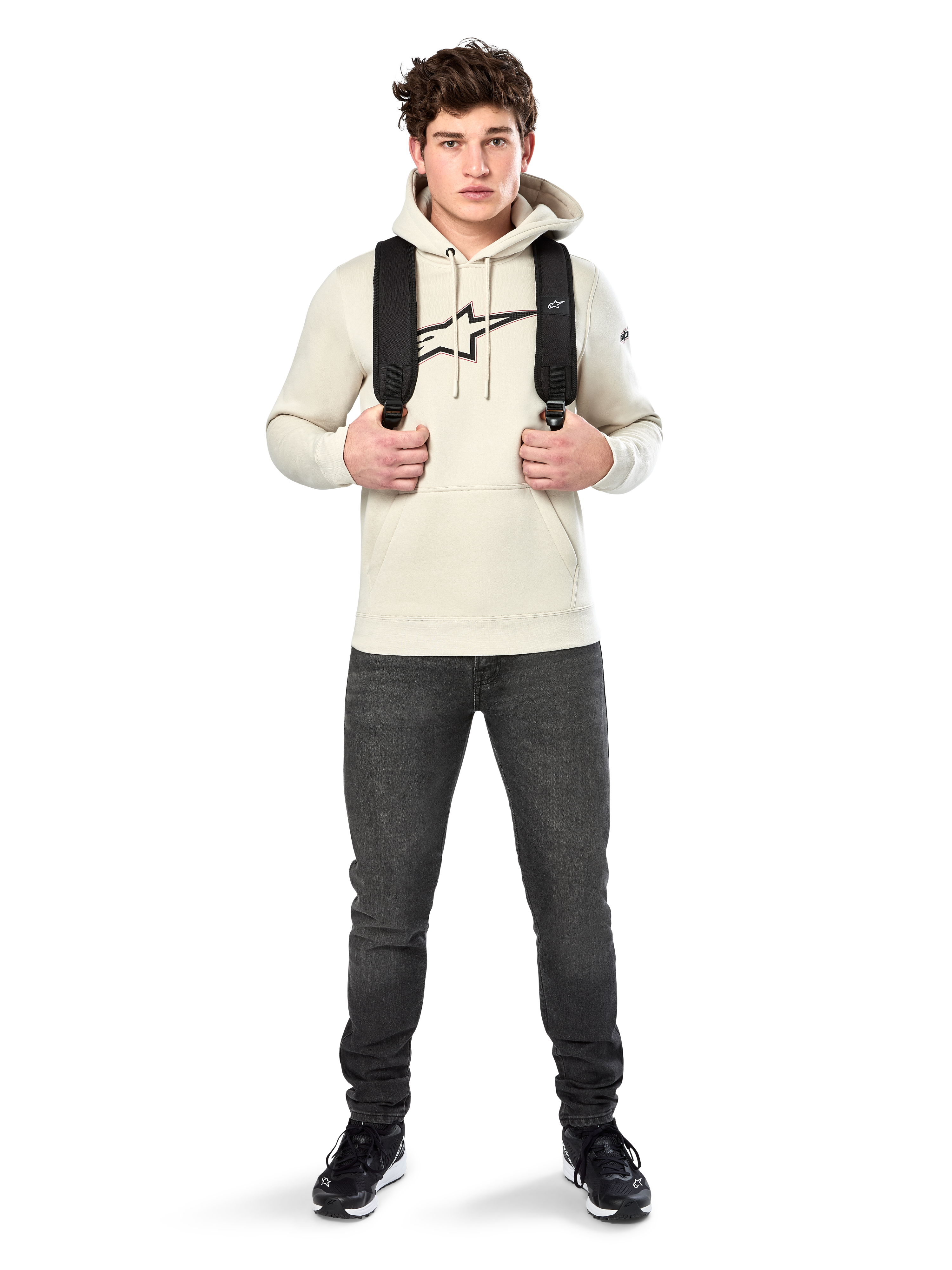 Alpinestars Insignia Hoodie, codzienna odzież streetwear, polarowa bluza w kolorze Off White, logo z motywem włókna węglowego i czerwonym konturem, kaptur ze sznurkiem, kieszeń kangurka, na modelu z czarnym plecakiem i ciemnoszarymi dżinsami