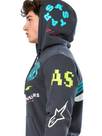 Bluza z kapturem Alpinestars Variegate, ciemnoszara polarowa bluza z zamkiem z przodu, profil boczny modelu, wielokolorowe grafiki z logo w kolorze neonowożółtym, jasnoniebieskim i białym, logo „AS” na rękawie i napis „STARS” na kapturze, codzienna odzież uliczna inspirowana sportami motorowymi