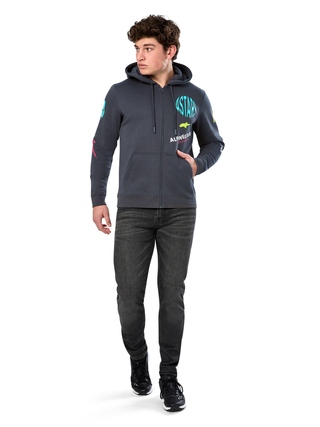 Alpinestars Variegate Hoodie, polarowa bluza z kapturem zapinana na zamek, kolor ciemnoszary (Gunmetal), noszona przez modela z czarnymi dżinsami i sneakersami, turkusowy napis „ASTARS” oraz kolorowe grafiki na rękawach i klatce piersiowej, codzienna odzież uliczna inspirowana sportami motorowymi