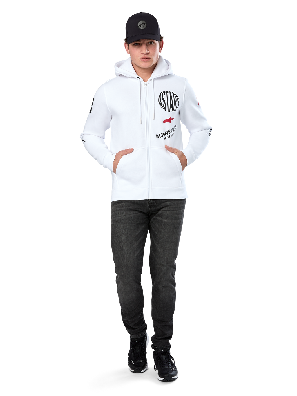 Bluza z kapturem Alpinestars Variegate, biała rozpinana bluza polarowa z kapturem, wieloelementowa grafika z napisem „ASTARS” i czerwonym logo gwiazdy na piersi, detale graficzne na rękawach, model w czarnej czapce z daszkiem i czarnych jeansach, codzienna odzież streetwear w stylu motorsport