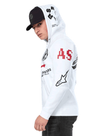 Alpinestars Variegate Hoodie, biała polarowa bluza z zamkiem z przodu, grafiki z wieloma logo na rękawach i kapturze, czerwony napis „AS” i czarne logo gwiazdy, noszona przez mężczyznę w czarnej czapce, codzienna odzież uliczna w stylu motorsport