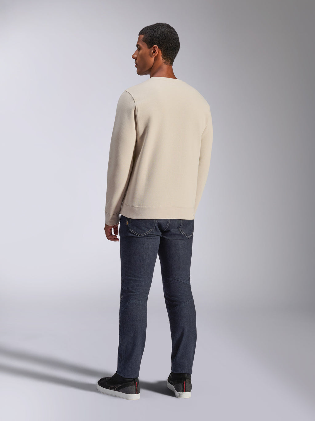 Alpinestars Positive Crew, bluza typu crewneck w kolorze złamanej bieli, widok z tyłu na modelu, w zestawieniu z ciemnymi jeansami i czarnymi sneakersami, casualowa odzież uliczna w stylu motorsport, ze ściągaczami przy mankietach i na dole