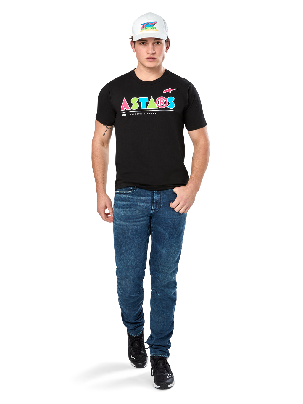Męski model ubrany w koszulkę Alpinestars Cereal CSF Tee, czarny T-shirt z krótkim rękawem z kolorowym geometrycznym logo ASTARS, zestawiony z niebieskimi jeansami i białą czapką, casualowy styl streetwear inspirowany motorsportem