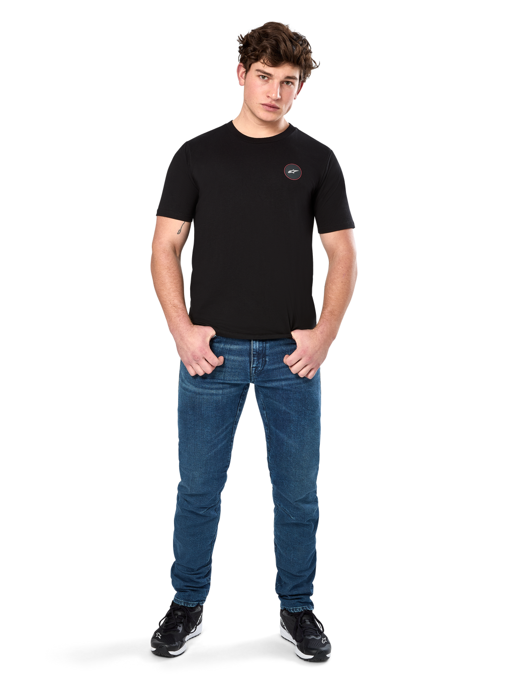 Alpinestars Dot Carbon CSF Tee, koszulka z krótkim rękawem, czarna, małe okrągłe logo Astars Dot na piersi, zestawiona z niebieskimi jeansami i czarnymi sneakersami, codzienna odzież streetwearowa w stylu motorsportowym