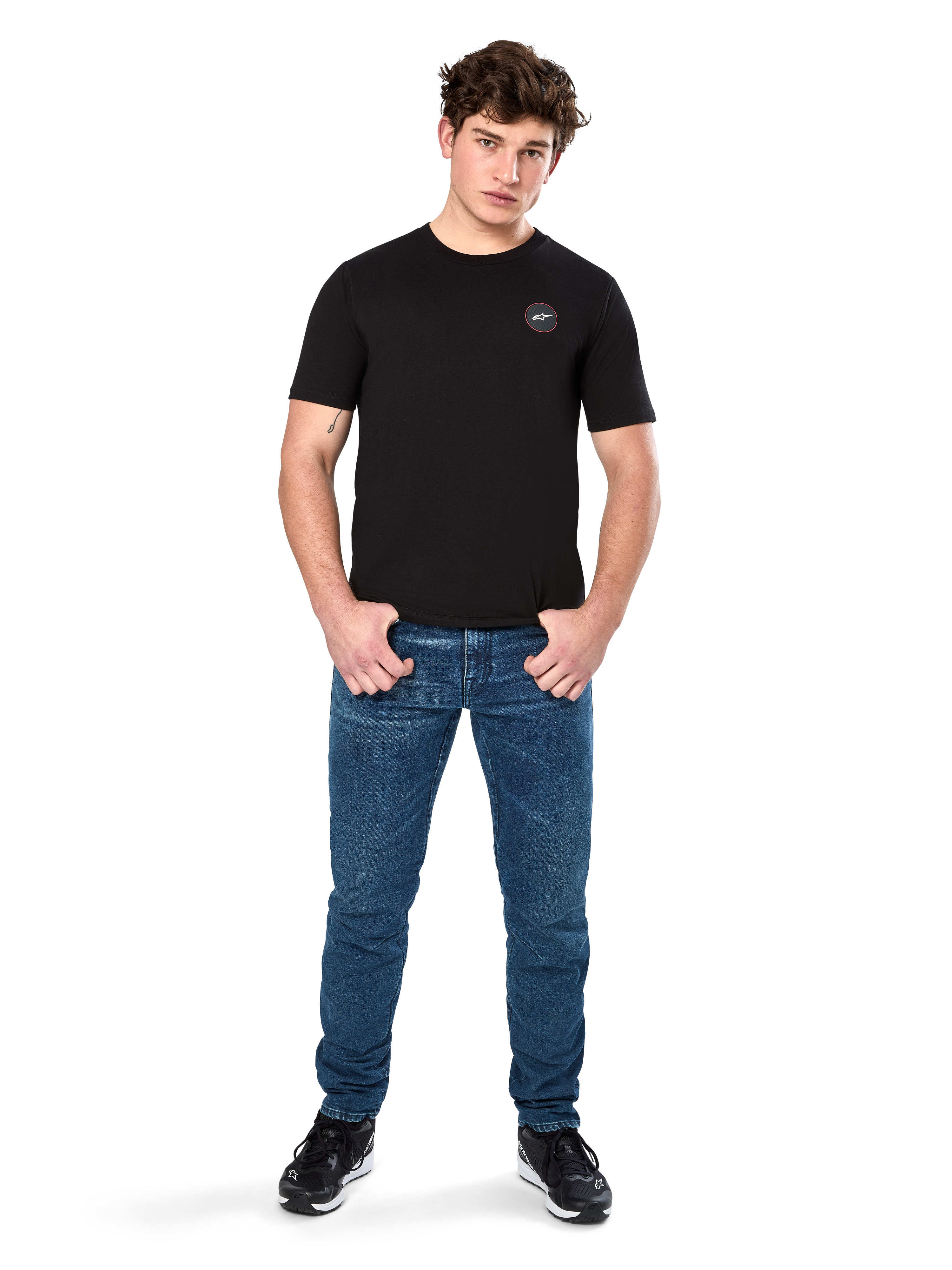 Alpinestars Dot Carbon CSF Tee, koszulka z krótkim rękawem, czarna, małe okrągłe logo Astars Dot na piersi, zestawiona z niebieskimi jeansami i czarnymi sneakersami, codzienna odzież streetwearowa w stylu motorsportowym