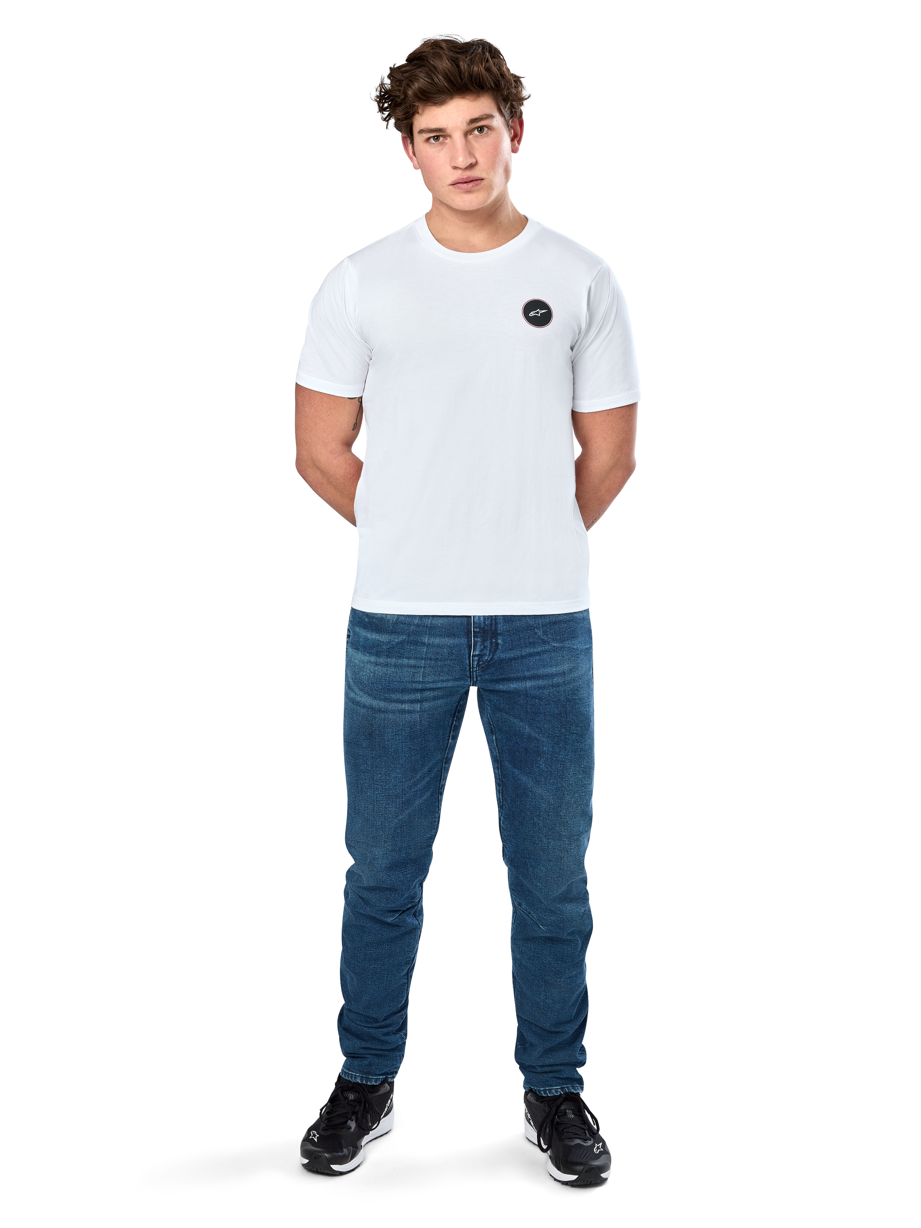 Alpinestars Dot Carbon Csf Tee, koszulka z krótkim rękawem, biała, okrągłe logo Astars o wyglądzie włókna węglowego, codzienna odzież uliczna w stylu motorsport, noszona przez modela w niebieskich jeansach i czarnych sneakersach