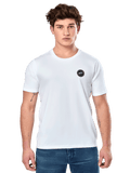 Alpinestars Dot Carbon CSF Tee, biała koszulka z krótkim rękawem, męski model w białej koszulce z małym czarnym okrągłym logo na piersi i niebieskich jeansach, casualowy styl motorsportowy