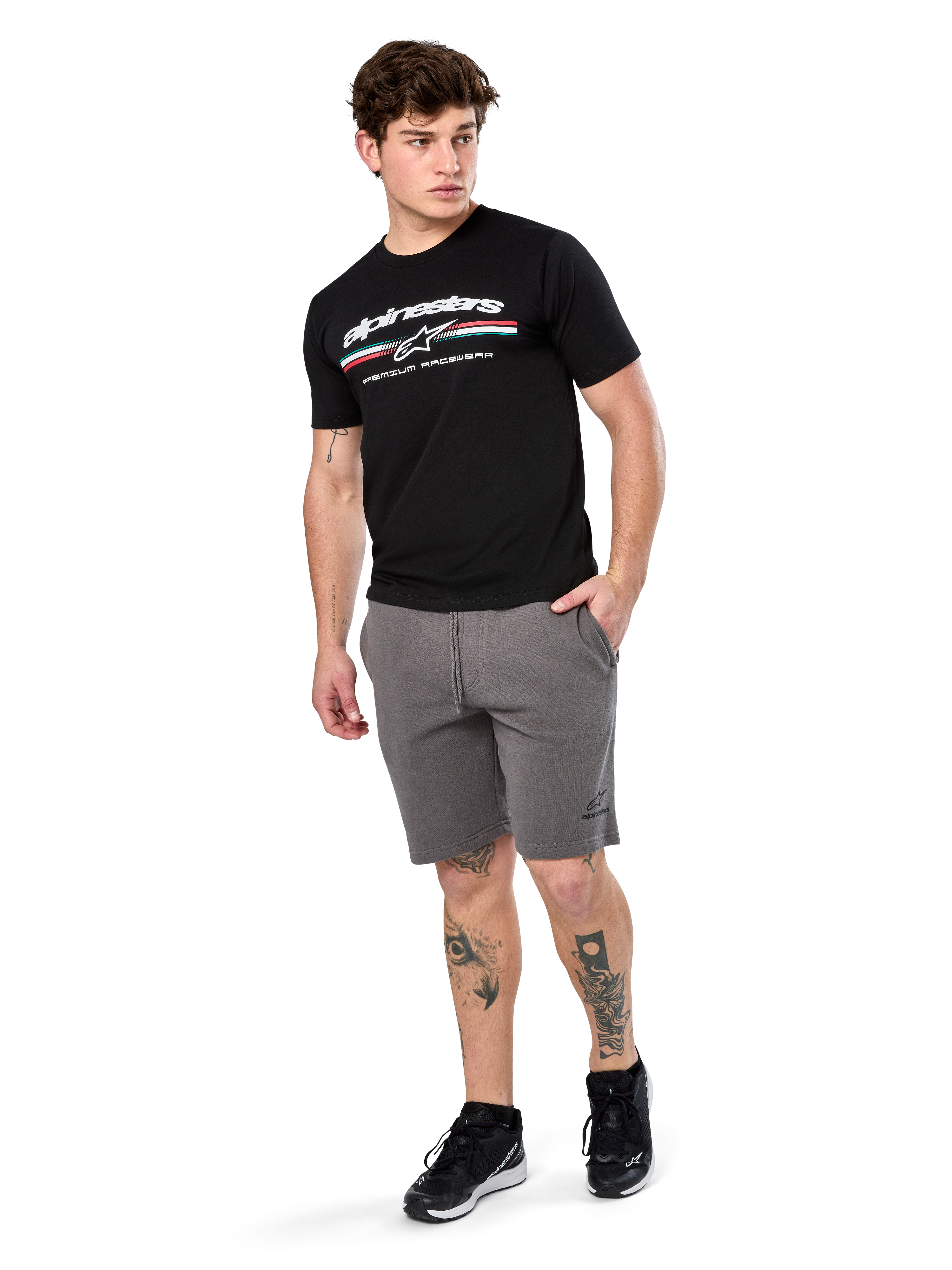 Alpinestars Prevail Csf Tee, koszulka z krótkim rękawem, czarna, białe logo Alpinestars z trójkolorowym paskiem w stylu paddock, noszona z szarymi szortami i czarnymi sneakersami, codzienna odzież streetwearowa w stylu motorsportowym
